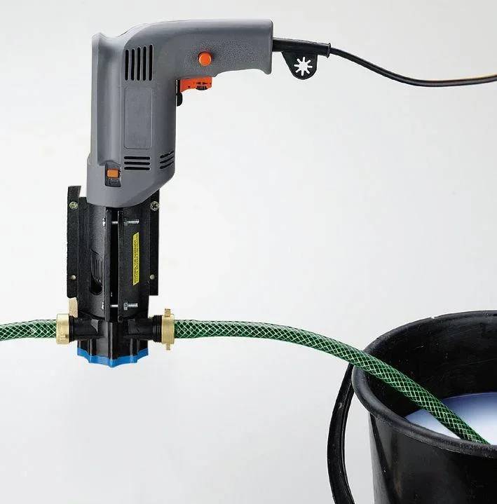 Ein Akkuschrauber mit einem angesetzten Farbmischer mischt eine blaue Flüssigkeit in einem schwarzen Eimer. Ein grüner Schlauch ist an den Mischer angeschlossen.