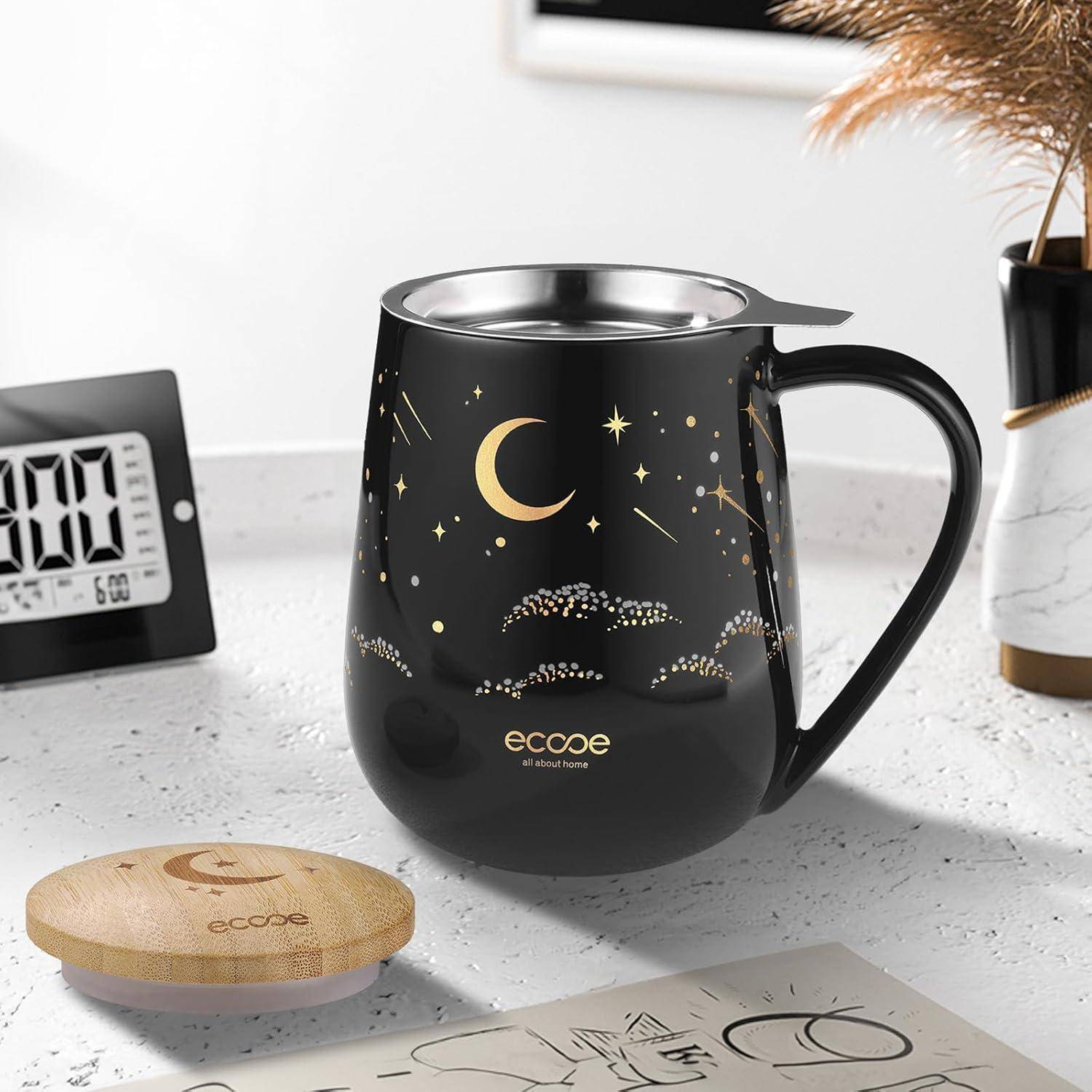 Eine schwarze Tasse mit Gold-Mond- und Sternenmustern steht auf einem Tisch neben einem Holzuntersetzer. Eine digitale Uhr ist im Hintergrund zu sehen.