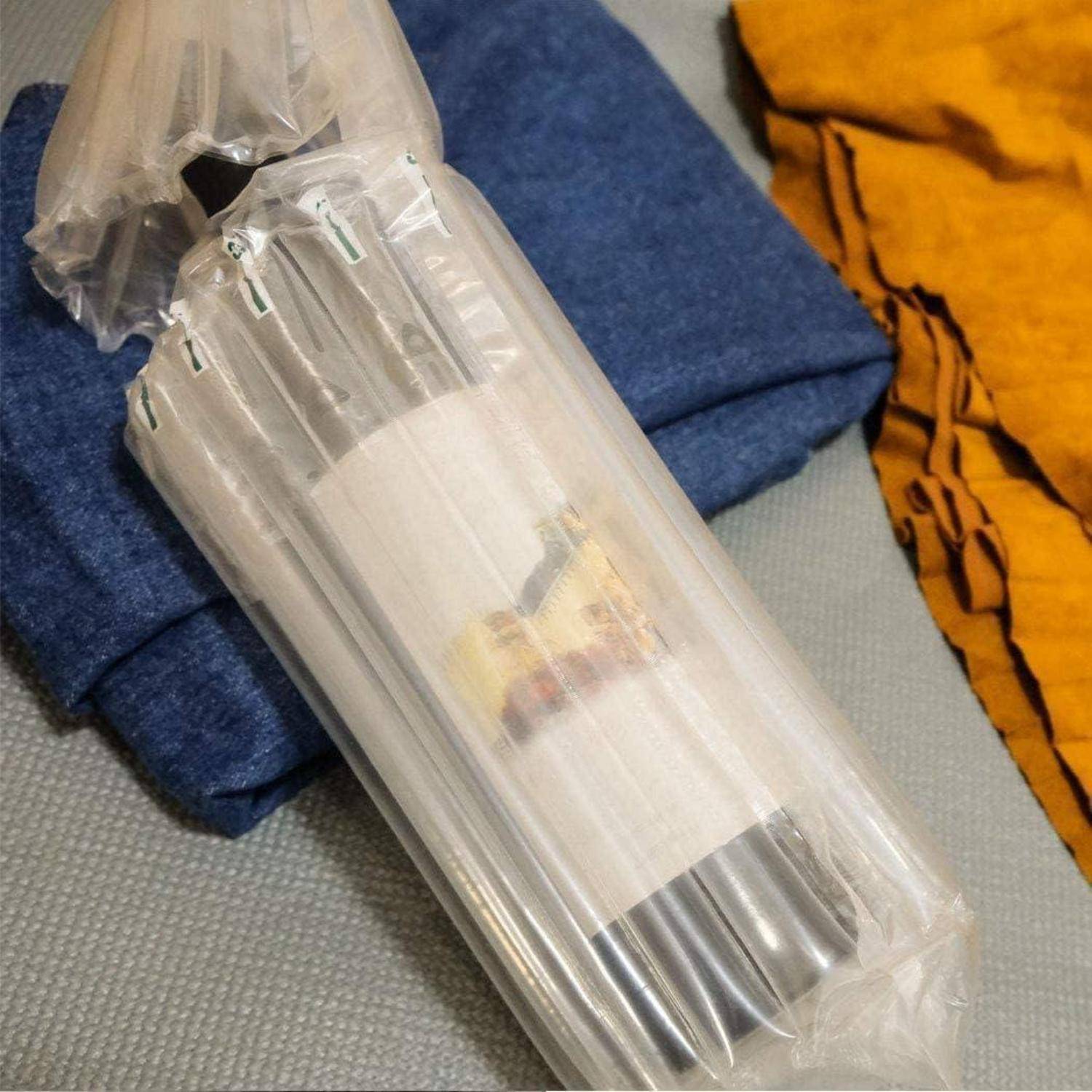 Eine Flasche, die in aufblasbare Schutzverpackung eingewickelt ist, wird auf zusammengefaltetem dunkelblauen Stoff platziert, mit einem senfgelben Stoff in der Nähe.