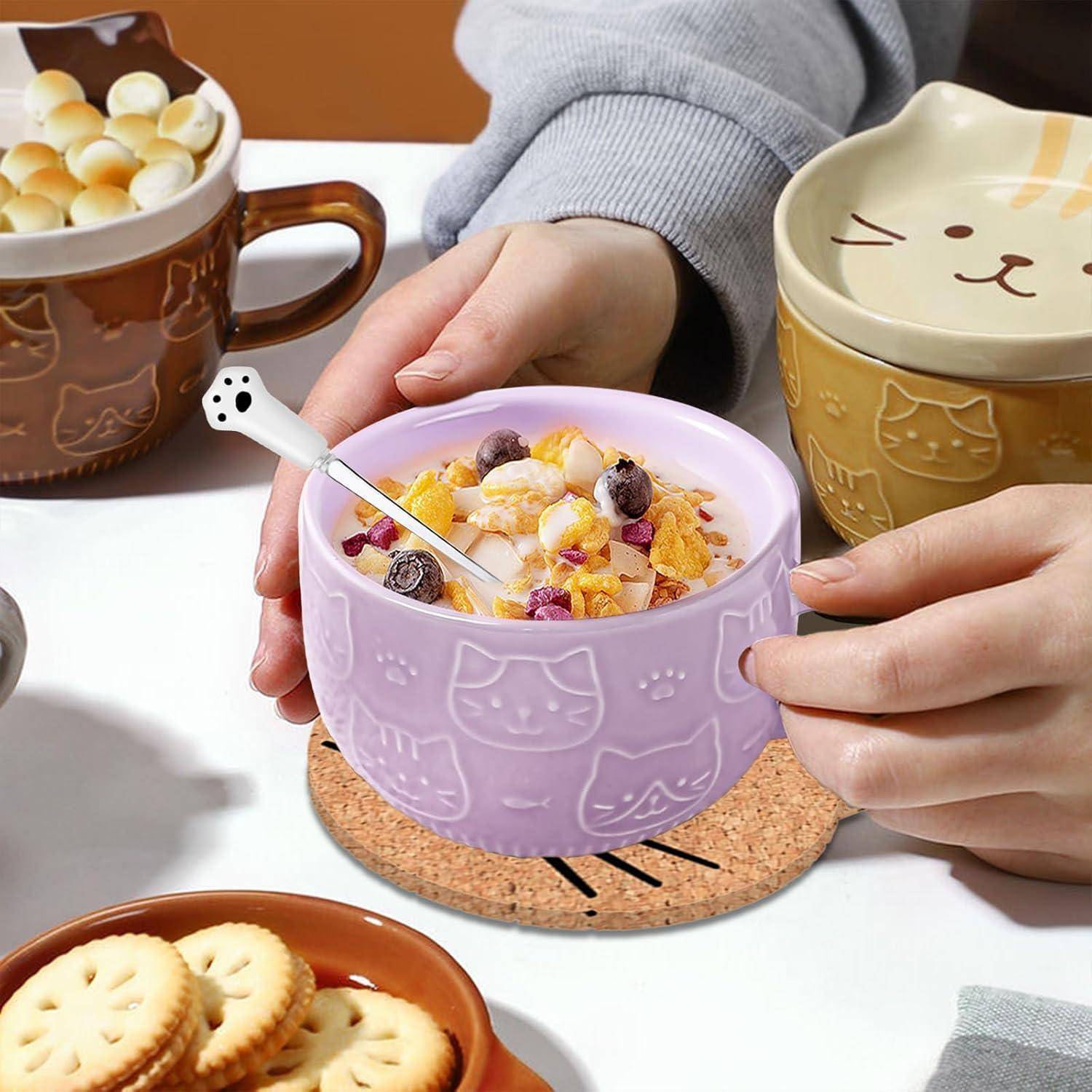 Eine Person hält eine lila Schüssel mit Katzenmustern, gefüllt mit Müsli, Obst und Milch. Das umgebende Geschirr umfasst eine Katzen-Tasse und einen Teller mit Keksen.