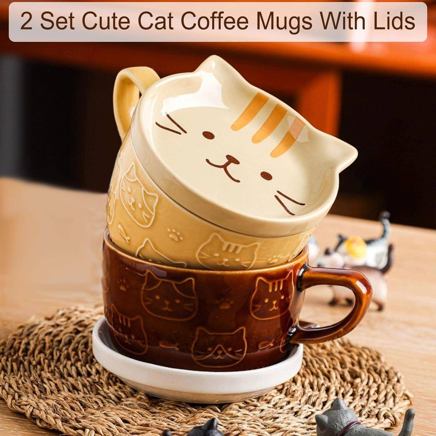 Zwei Kaffeetassen aus Keramik mit Katzendesigns und passenden Deckeln, eine gelb und eine braun, gestapelt auf einem Tisch. Text lautet '2er Set Süße Kaffeetassen mit Katzen-Motiv und Deckel'.