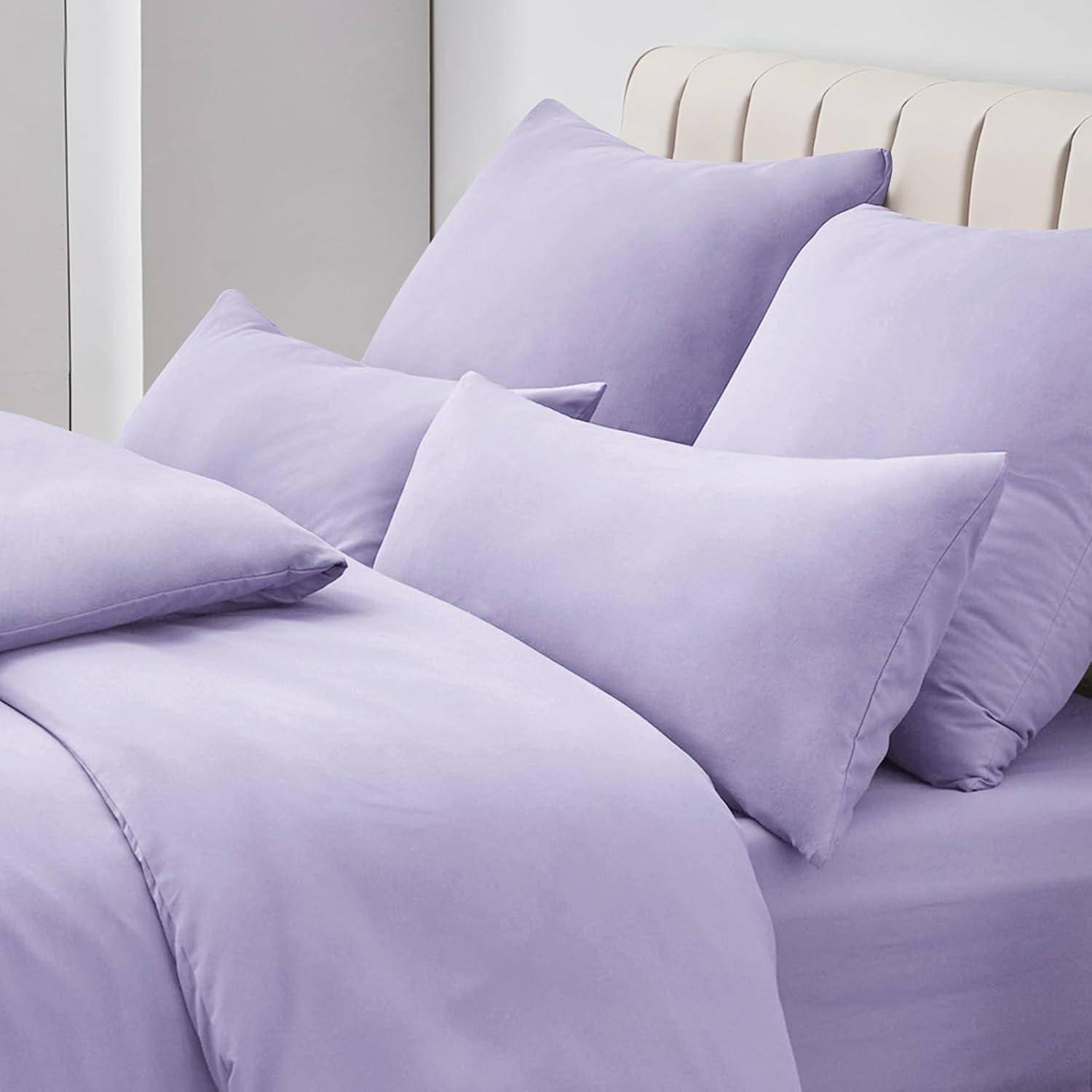 Ein ordentlich gemachtes Bett mit pastellfarbenen lila Bettwäsche und Kissen in einem hellen Raum, der eine ruhige und einladende Atmosphäre schafft.