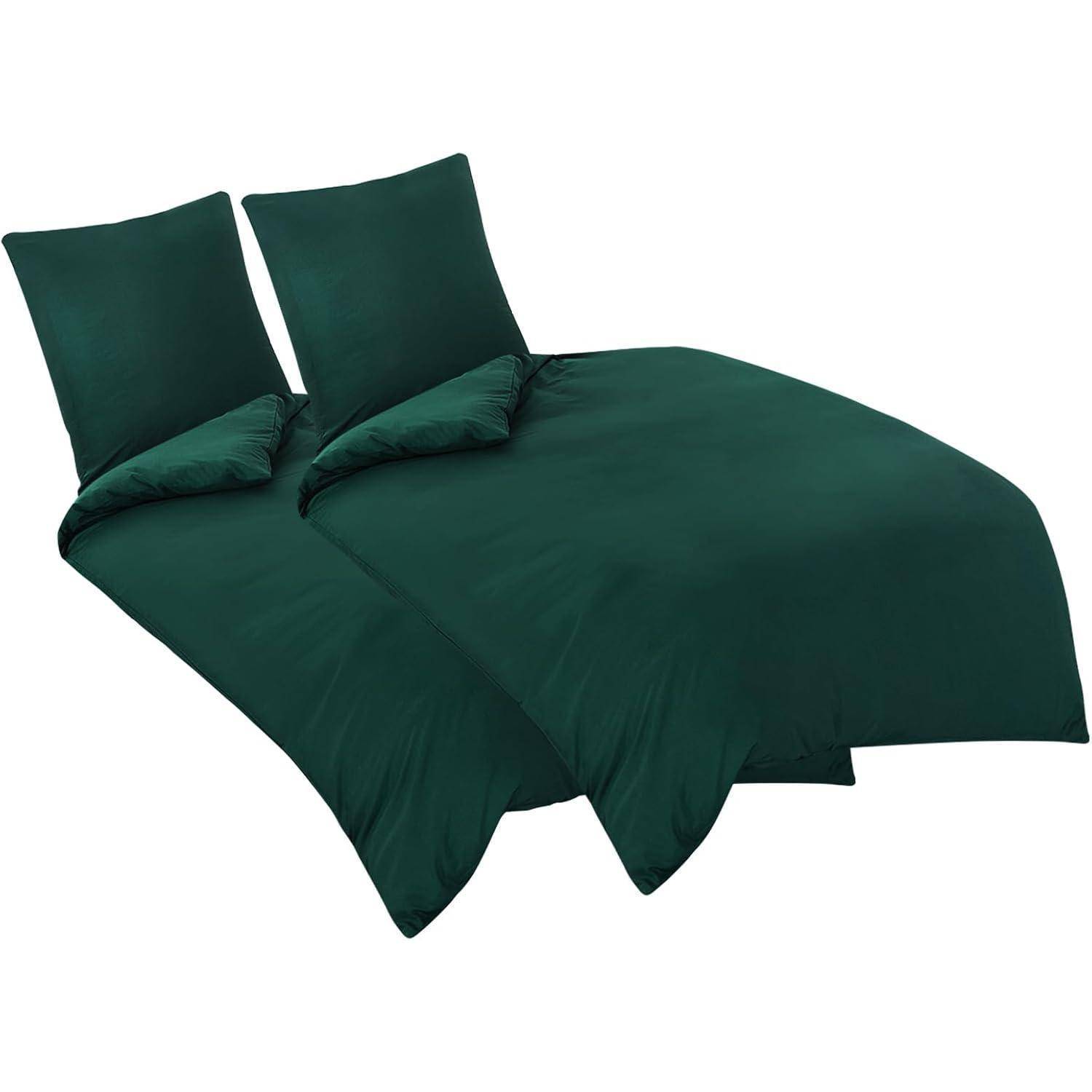 Zwei dunkelgrüne Kissen und ein passender Bettdeckenbezug auf einem Bett, die ein schlichtes und elegantes Bettwäschedesign vermitteln.