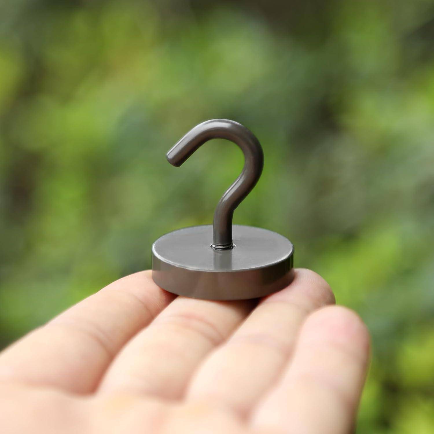 Eine Hand hält einen kleinen, runden, metallischen Haken vor einem unscharfen grünen Hintergrund.
