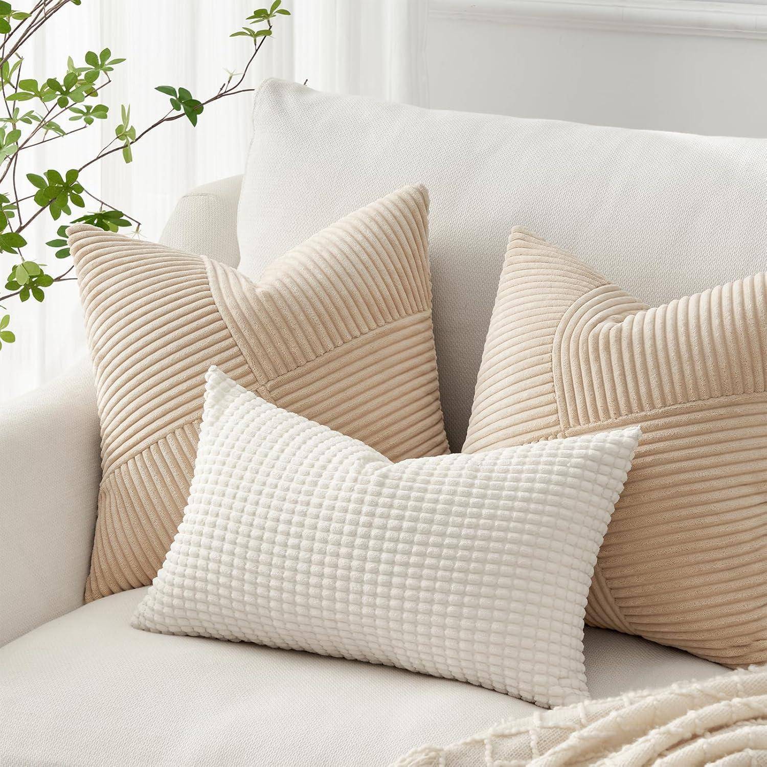 Drei beige Kissen mit dezenten Mustern auf einem weißen Sofa, umgeben von einigen grünen Pflanzen im Hintergrund.