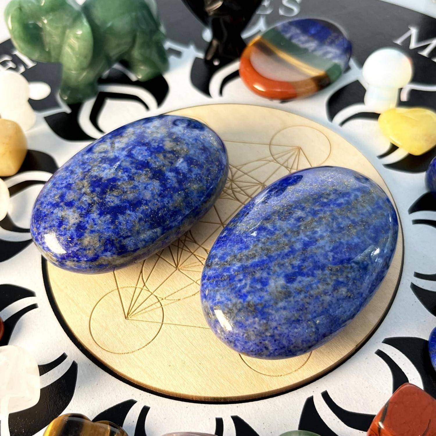 Zwei blaue Lapislazuli-Steine ruhen auf einem kreisförmigen Holzbrett mit einem geometrischen Muster, umgeben von verschiedenen kleinen polierten Steinen.