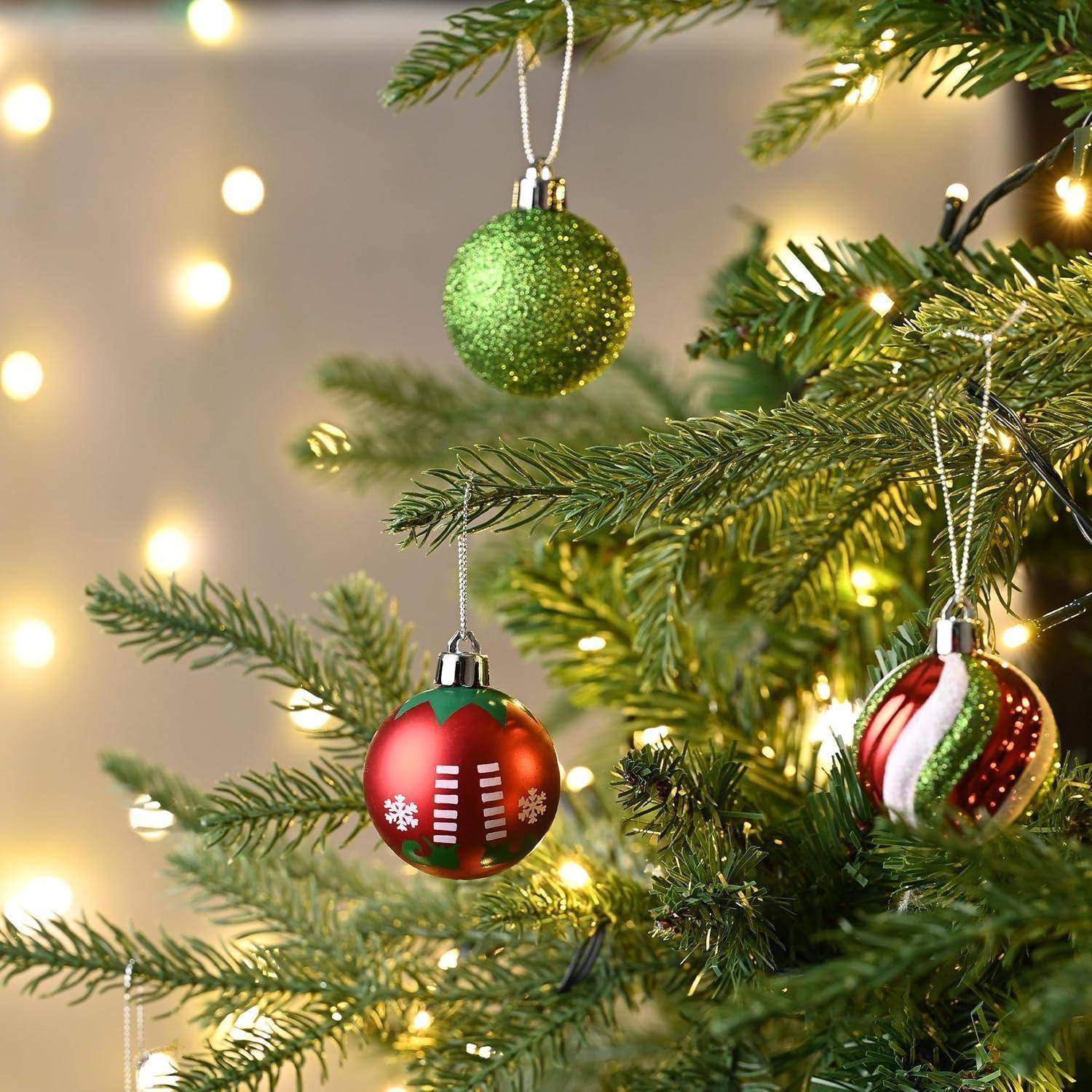 Ein Weihnachtsbaum mit grünen und roten Weihnachtskugeln, darunter eine grüne glitzernde Kugel, eine rote Kugel mit Schneeflocken und eine rot-weiß gestreifte Kugel, ist mit Lichterketten geschmückt.