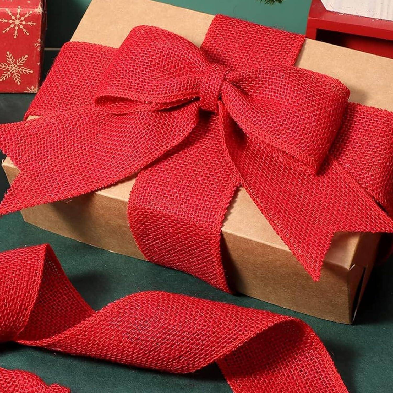 Eine Geschenkbox aus Karton, umwickelt mit einem großen roten Juteband, auf einer grünen Oberfläche platziert.