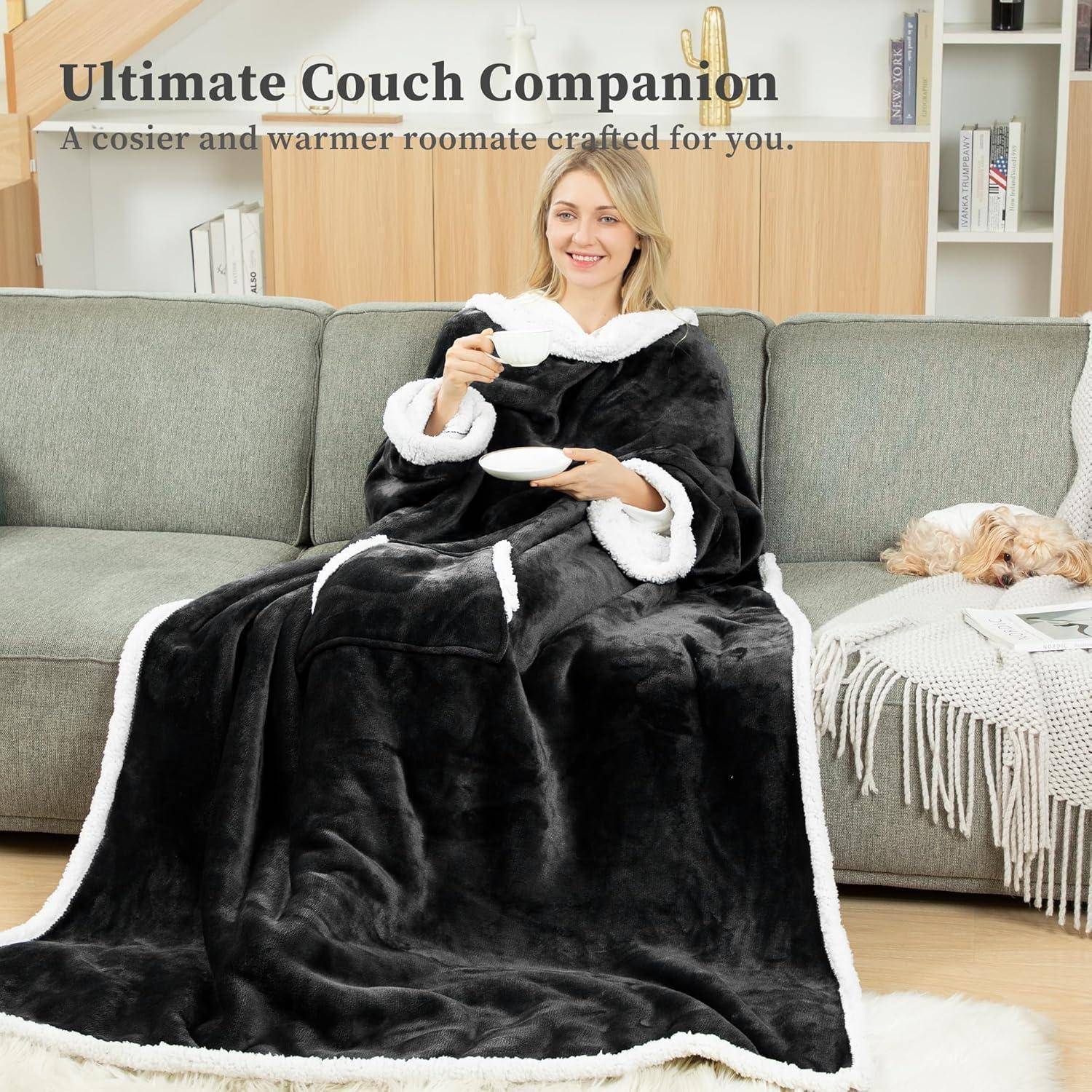 Eine Person sitzt auf einer Couch, in eine gemütliche, schwarze Fleece-Decke mit Taschen gehüllt, und trinkt aus einer Tasse. Text darüber liest sich: 