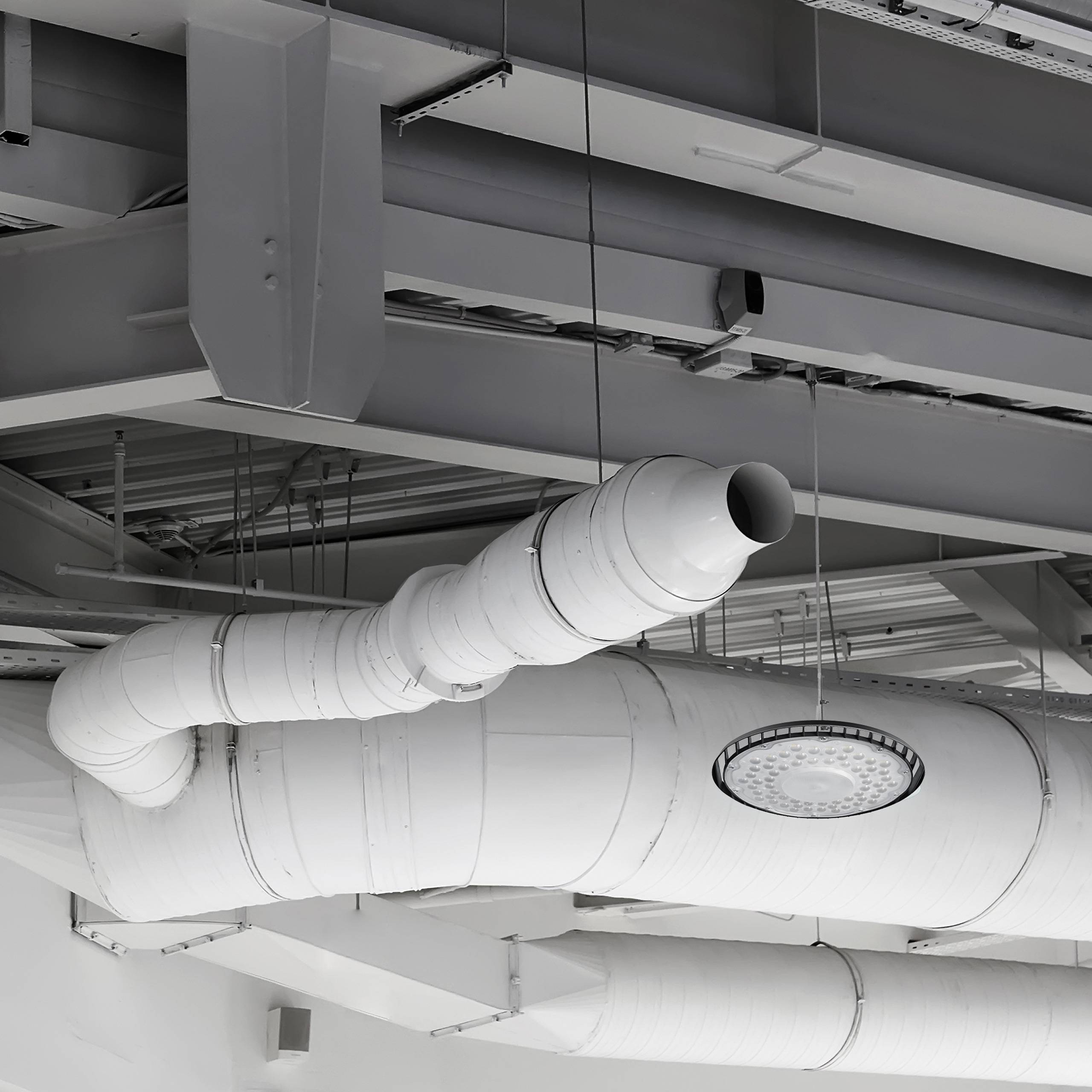 Industrielle Decke mit Luftkanälen, einem großen runden Lüftungsschacht und freigelegten Trägern in einem modernen Gebäude.