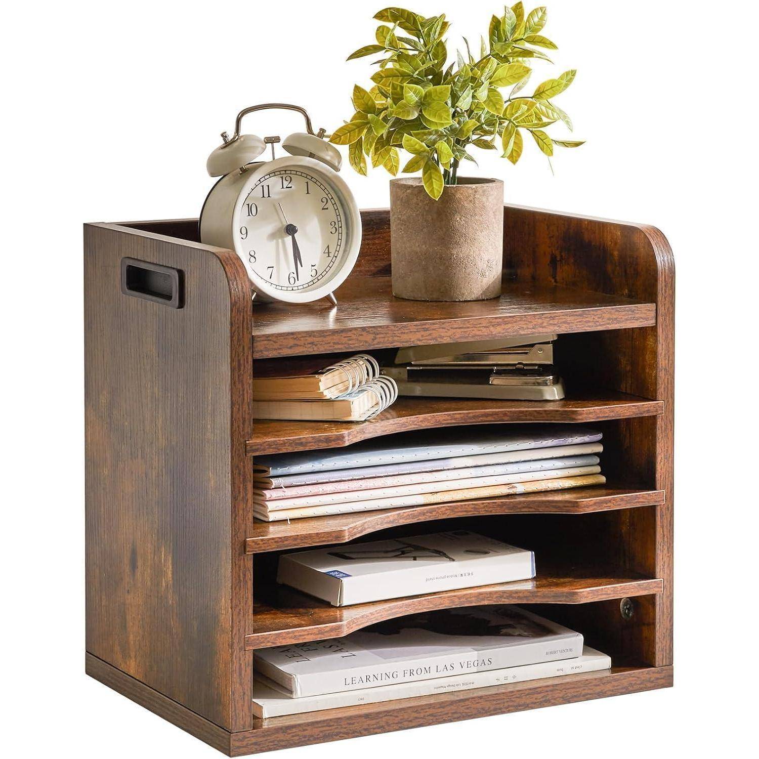 Ein Schreibtisch-Organizer aus Holz mit vier Ablagen enthält verschiedene Papiere, Zeitschriften und eine kleine Topfpflanze. Ein Wecker steht oben drauf.