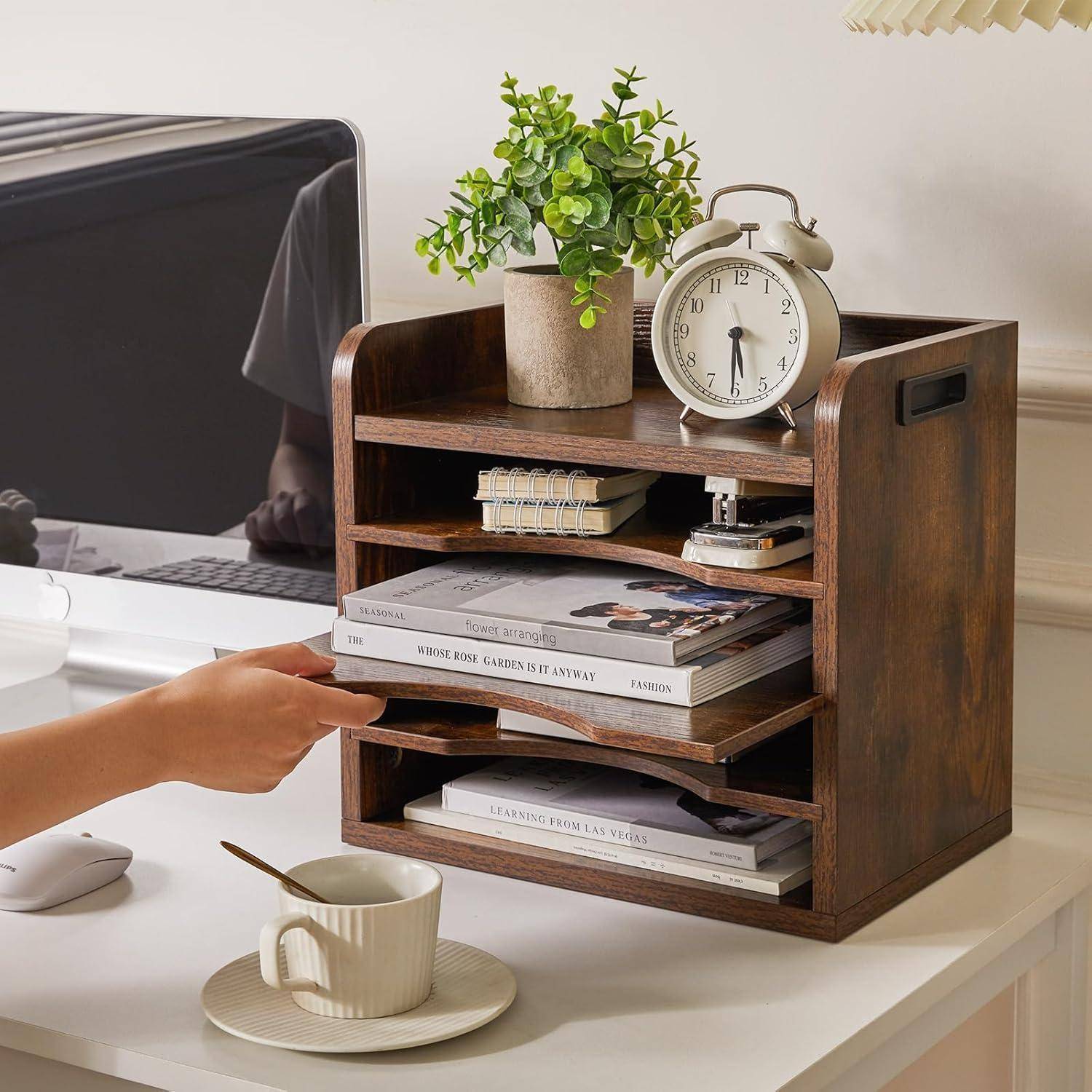 Eine Hand öffnet eine Schublade in einem Holz-Schreibtischorganizer, der Bücher, eine Pflanze und eine Uhr enthält. Eine Tasse und ein Computer befinden sich auf dem Schreibtisch.