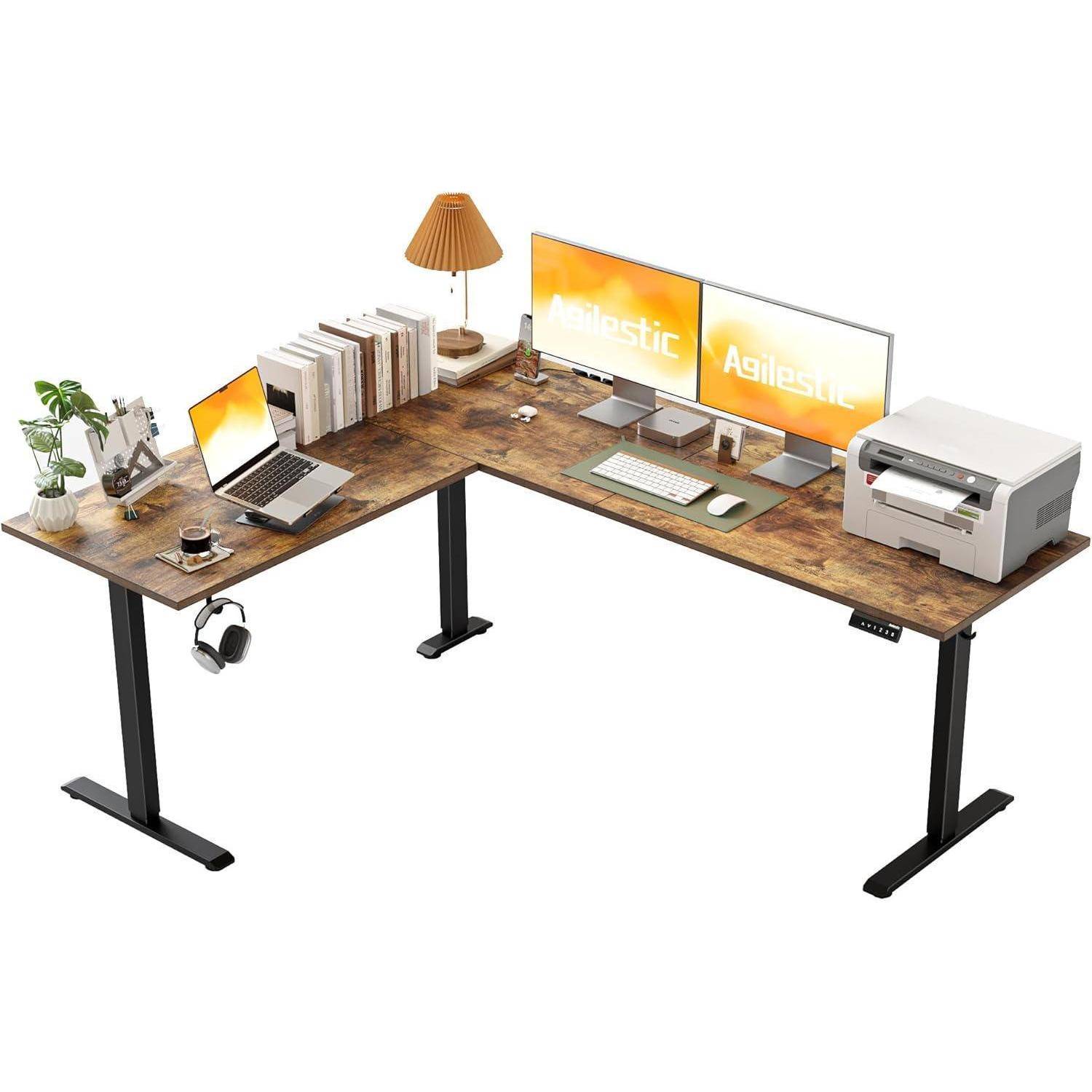 L-förmiger Stehschreibtisch-Aufbau mit zwei Monitoren, Laptop, Pflanze, Büchern, Kopfhörern und Drucker, der einen organisierten Arbeitsbereich bietet.