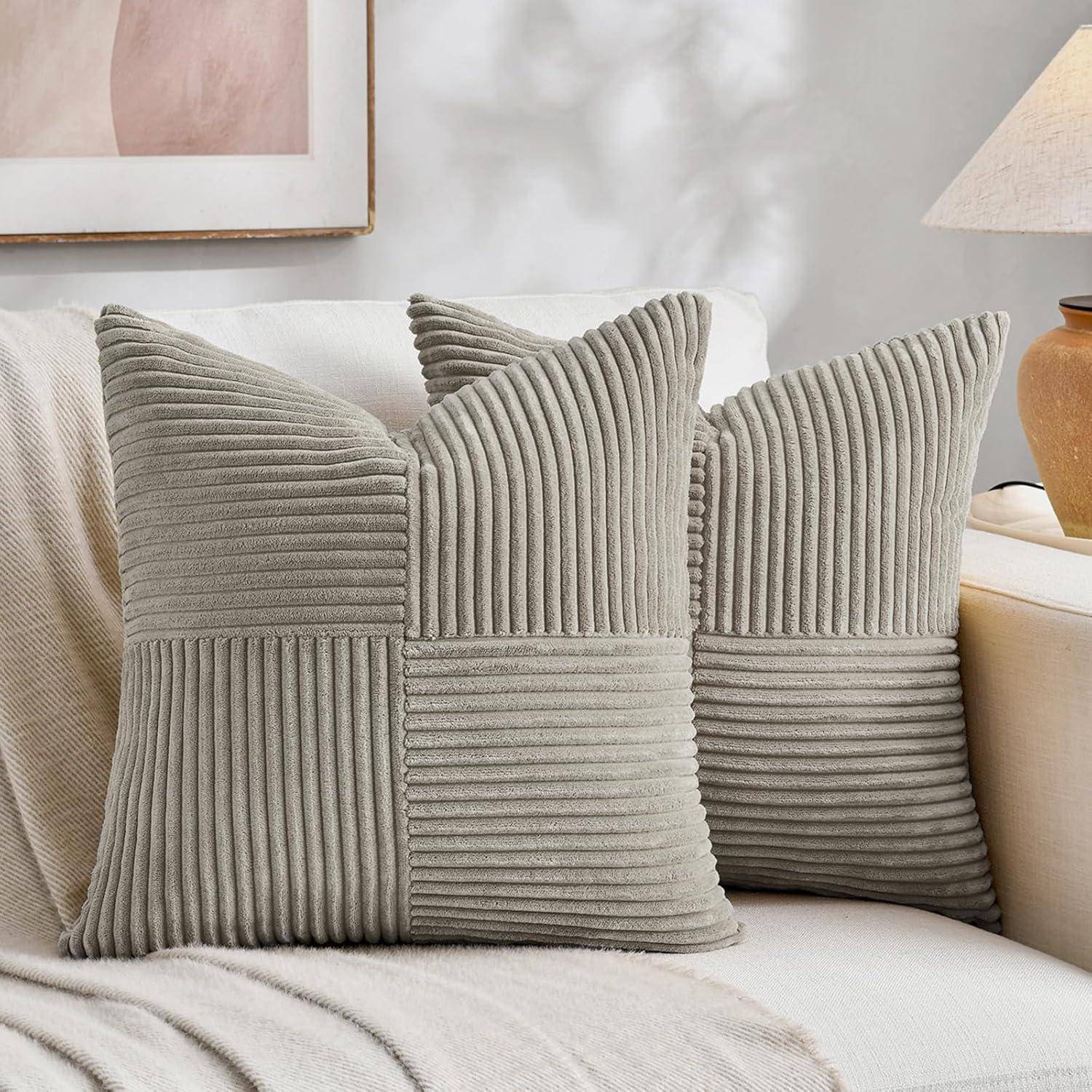 Zwei quadratische graue Cordkissen mit einem Steppdesign liegen auf einem beigen Sofa. Ein weiches Licht beleuchtet die Szene und schafft eine gemütliche Atmosphäre.