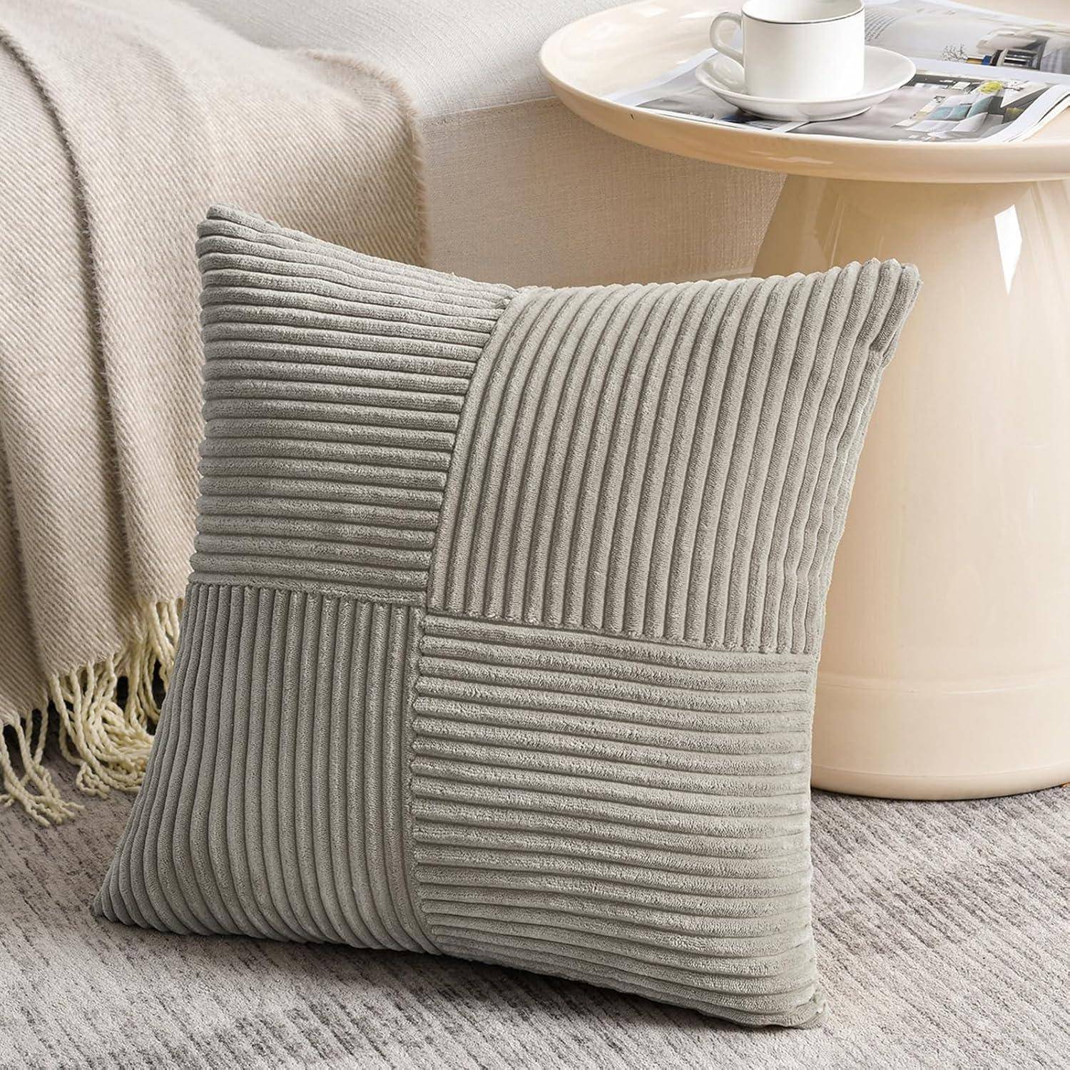 Ein strukturierter grauer Kissen lehnt an einem hellgefärbten Sofa. Ein rundes, hellholzfarbenes Couchtisch mit einer Tasse und einer Zeitschrift steht in der Nähe.