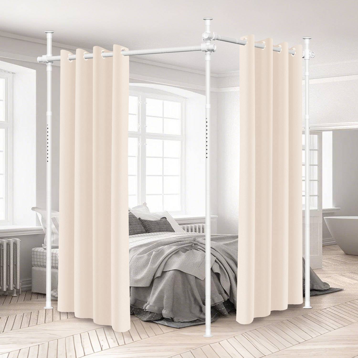 Raumteiler mit beigen Vorhängen trennt ein Bett vom Rest eines hellen Zimmers mit weißen Wänden und großen Fenstern.