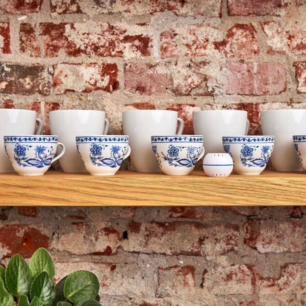 Keramiktassen und -schüsseln mit blauen Blumenmustern auf einem Holzregal vor einer Ziegelwand; kleine grüne Pflanze unterhalb des Regals.