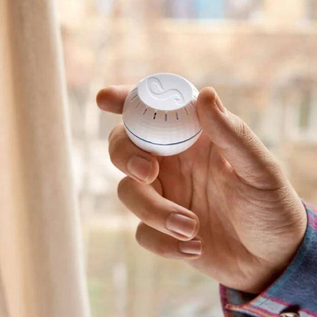 Eine Hand passt ein weißes Smart-Thermostat mit elegantem Design an, drinnen, nahe einem Fenster.