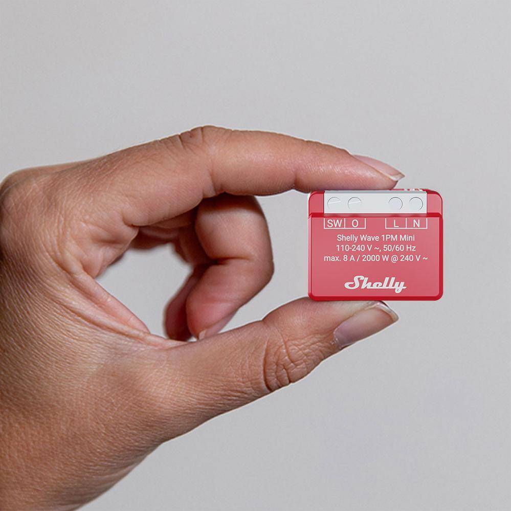 Eine Person hält ein kleines, rotes Shelly Wi-Fi Smart-Home-Gerät mit der Bezeichnung 'Shelly 1PM Mini', das zur Überwachung des Stromverbrauchs dient.