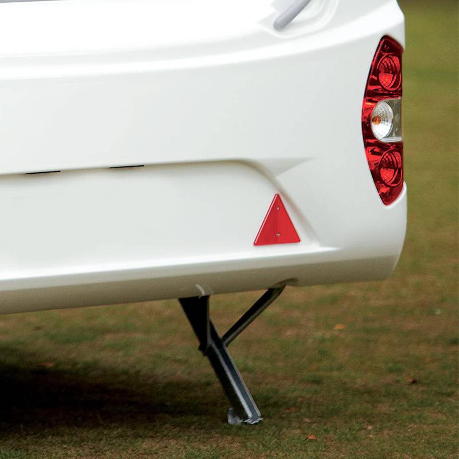 Weißer Wohnwagen von hinten, auf einem Stützgestell auf Gras ruhend. Das Rücklicht und ein dreieckiges reflektierendes Warnschild sind sichtbar.