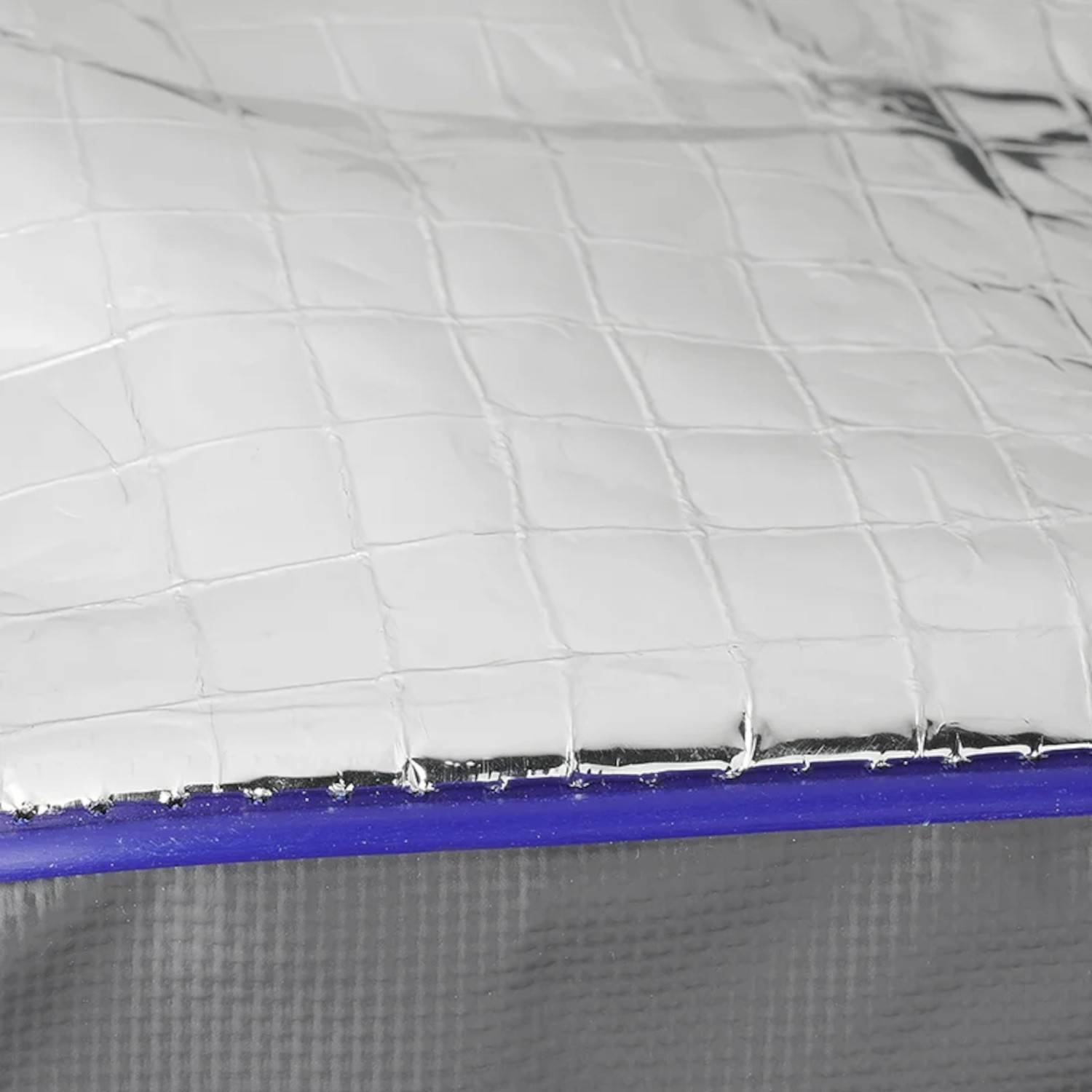 Nahaufnahme eines strukturierten, metallischen Gittermusters auf einer Oberfläche mit blauem Rand, was auf ein Isoliermaterial hindeutet.