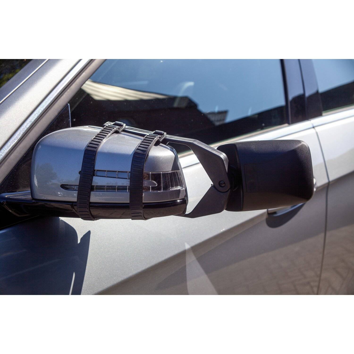 Ein beschädigter Autospiegel ist vorübergehend mit schwarzen Gurten gesichert, die an der Seite eines silbernen Fahrzeugs befestigt sind.