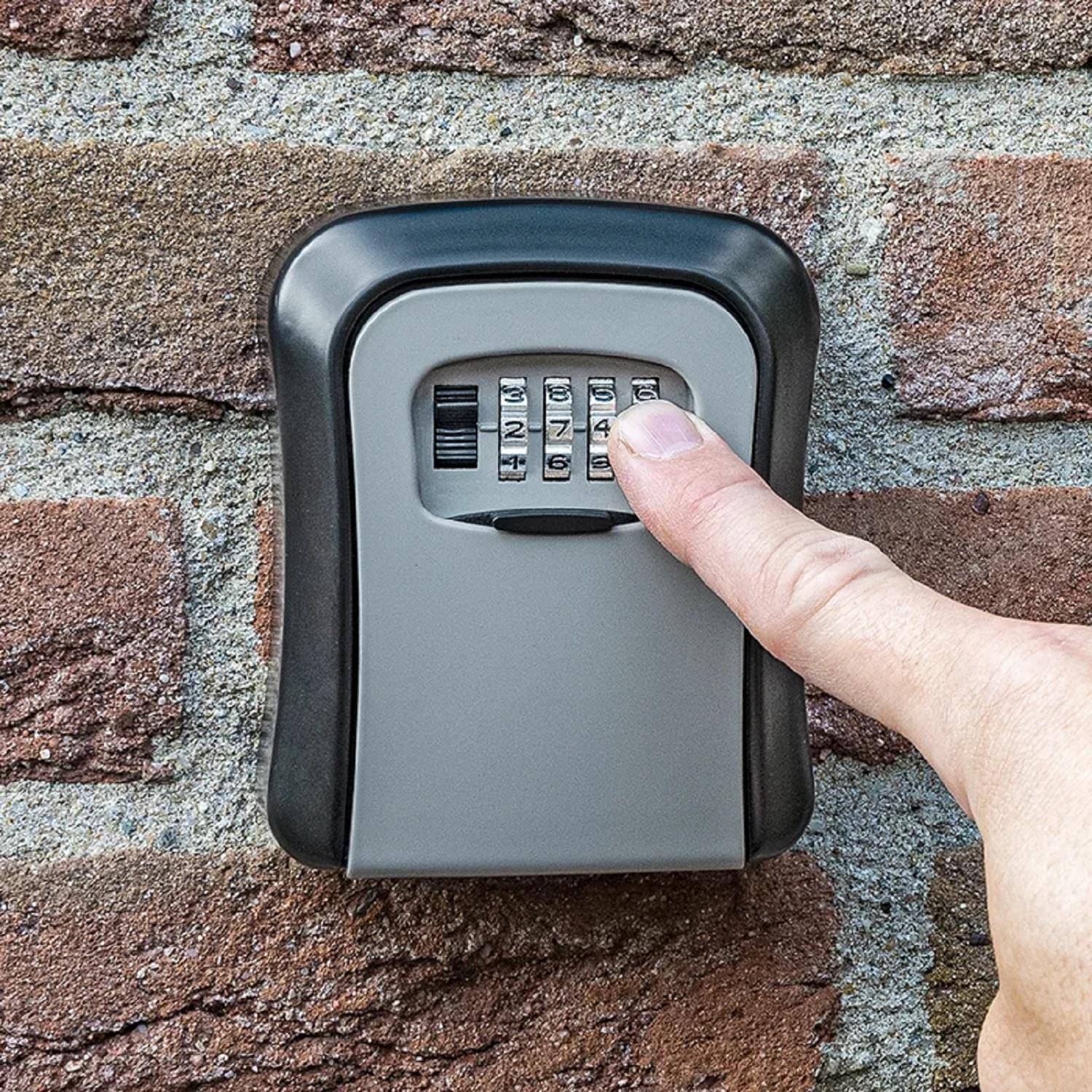 Eine Hand gibt eine Kombination auf einem an einer Ziegelwand montierten Zahlenschloss mit Zifferntastatur ein.