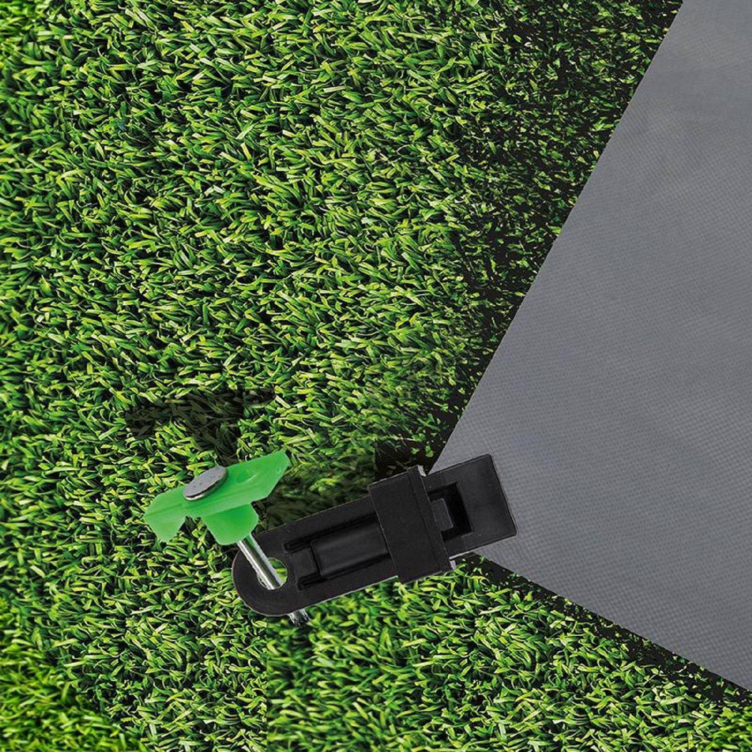 Nahaufnahme eines grünen Zeltherds, der den Rand eines grauen Campingzelts am Boden mit Gras befestigt.