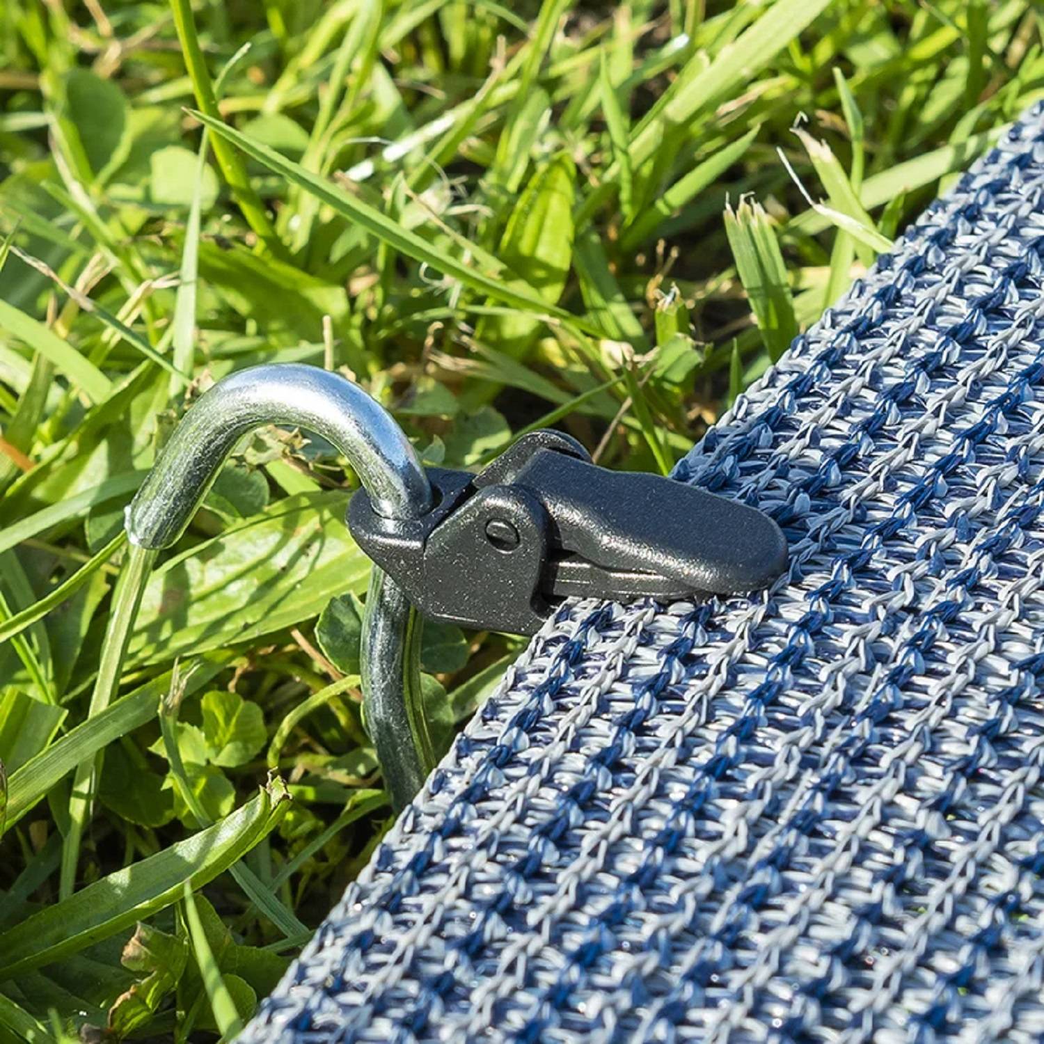 Ein Metallhaken befestigt eine blaue gewebte Matte am Gras und hält sie an Ort und Stelle.