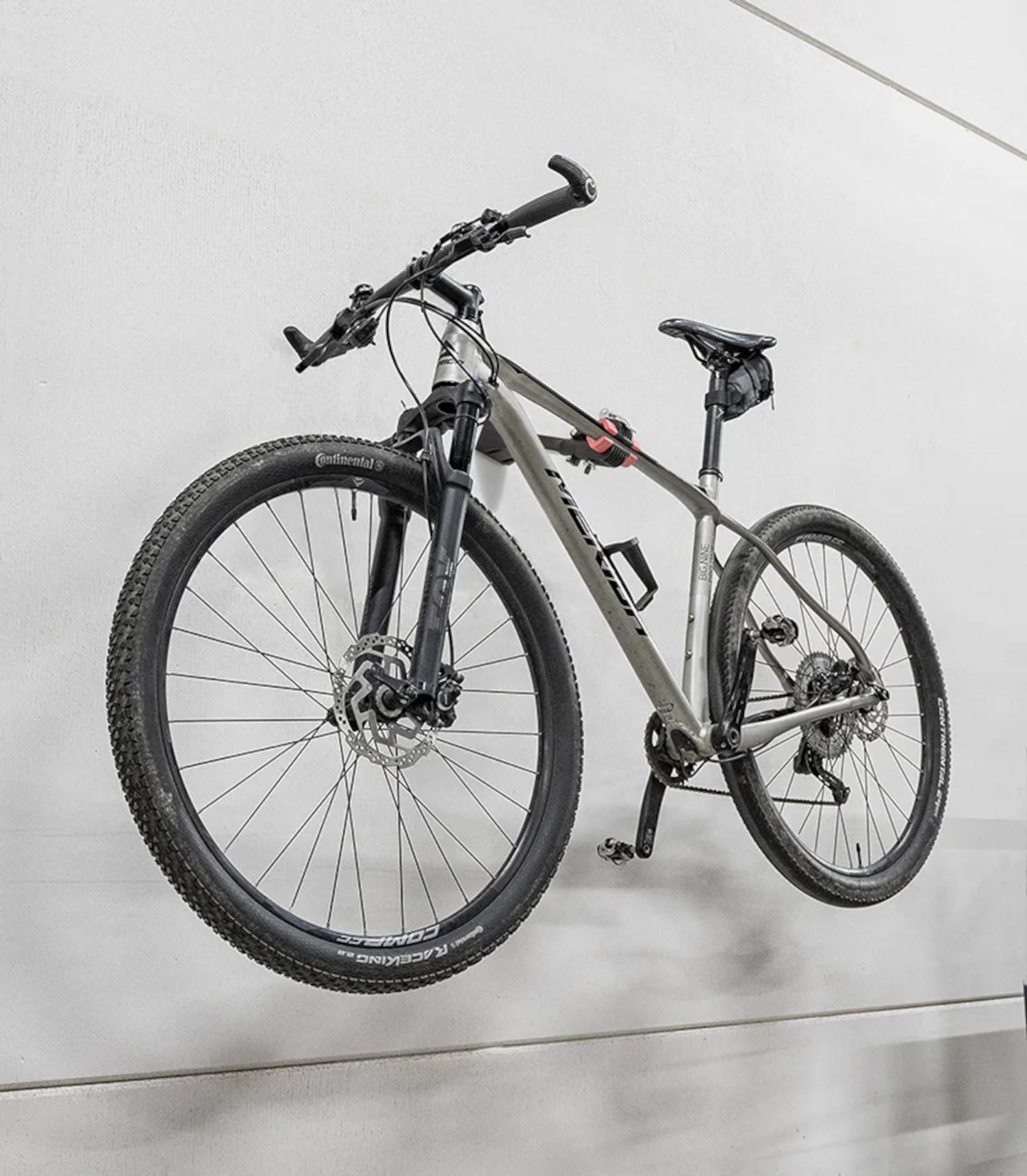 Ein Fahrrad, das senkrecht an einer Wand montiert ist, mit Scheibenbremsen und einem hellgrauen Rahmen.