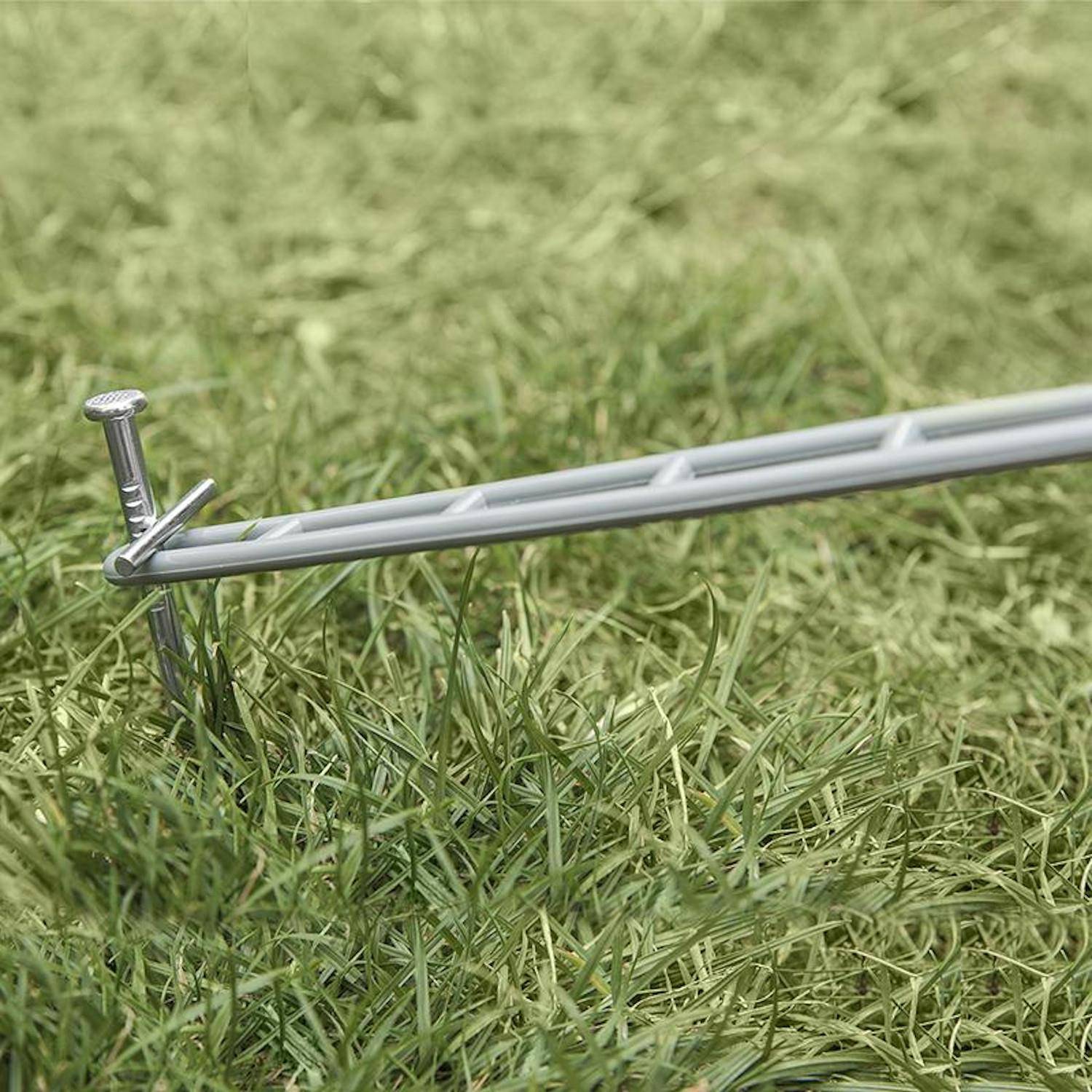 Ein Zeltheringe aus Metall sichert einen Pflock im Grasland und zeigt, wie man ein Zelt oder eine Freiluftstruktur stabilisiert.