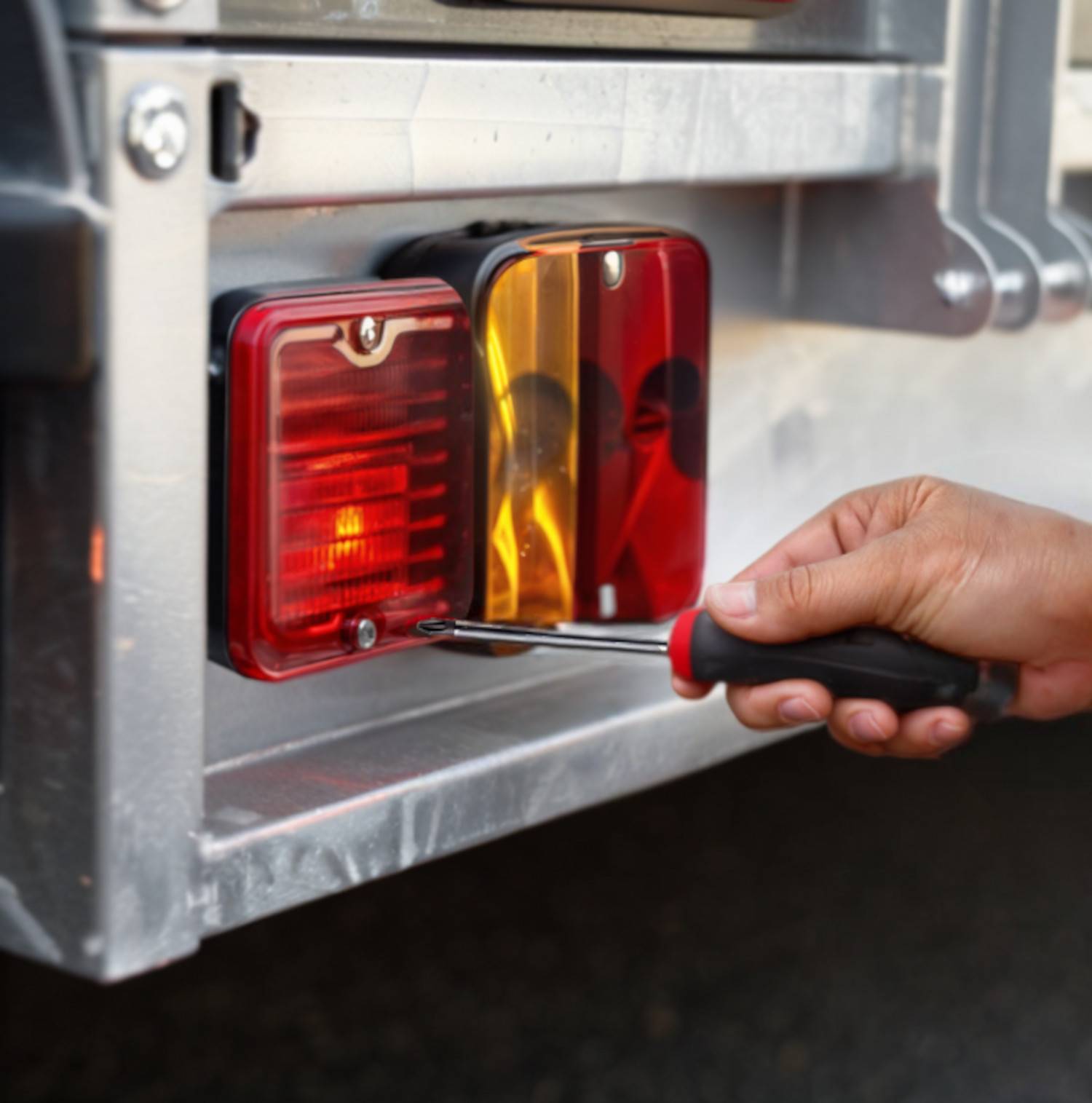 Eine Person verwendet einen Schraubendreher, um ein Rücklicht an einem Fahrzeug oder Anhänger zu befestigen, was auf Wartungs- oder Reparaturarbeiten hinweist.