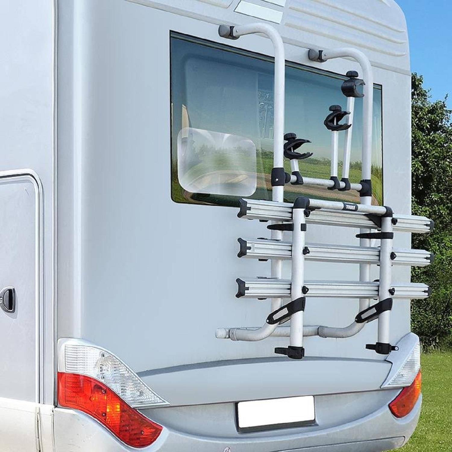Rückansicht eines weißen Wohnmobils mit einem Fahrradträger, der auf Gras geparkt ist. Ein Baum und ein klarer Himmel sind im Hintergrund sichtbar.