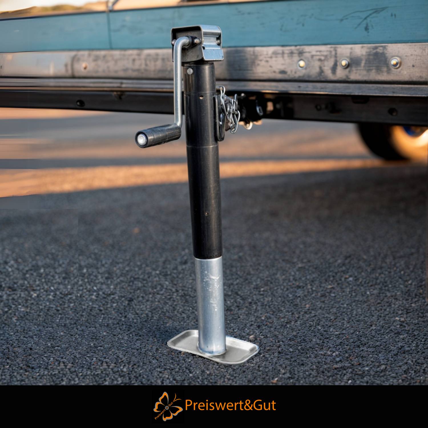 Ein Nahaufnahmebild eines Metall-Anhängerhebers auf Asphalt, der zur Stabilisierung von Anhängern verwendet wird. Ein Logo mit dem Text „Preiswert&Gut