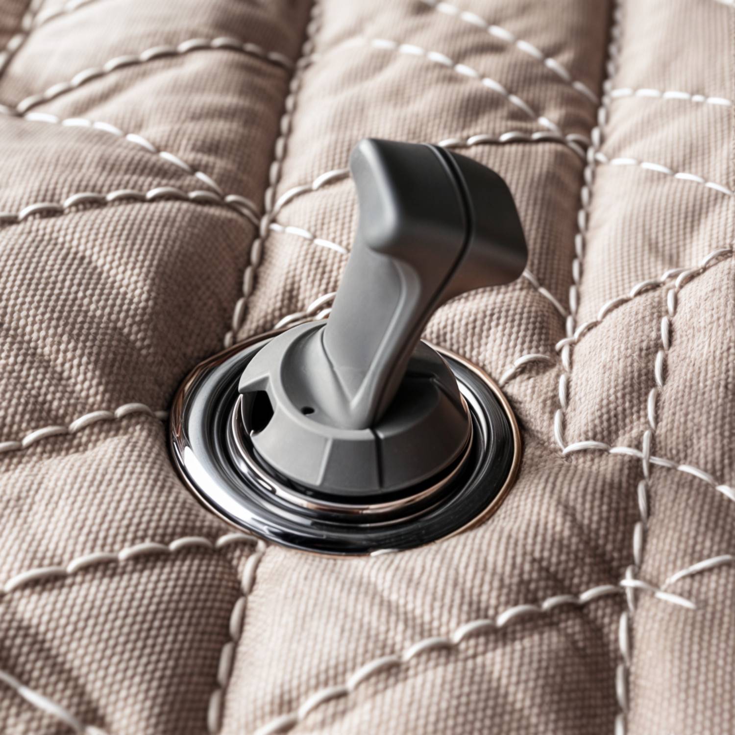 Eine Nahaufnahme eines schwarzen Kippschalters auf einer gesteppten Stoffoberfläche, die Stickdetails und Textur hervorhebt.