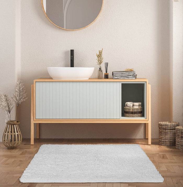 Ein modernes Badezimmer mit einem Waschtisch aus Holz, rundem Spiegel und Zimmerpflanzen. Ein kleines offenes Regal trägt zusammengefaltet Handtücher; dezente Dekoration verstärkt die Wärme.