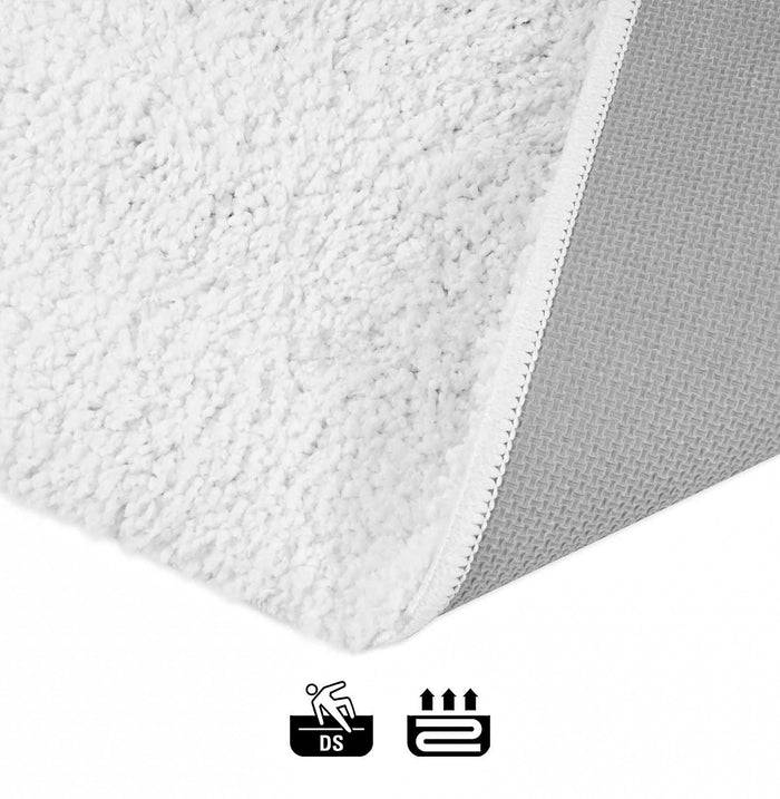 Detailaufnahme eines weißen Gewebes mit strukturierter Oberfläche und gewebtem Rand, daneben Symbole, die anzeigen, dass es beidseitig verwendbar und maschinell waschbar ist.