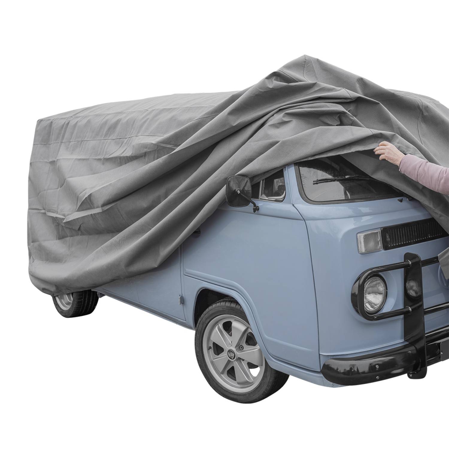 Ein blauer Oldtimer-Van ist im Freien geparkt und teilweise von einer grauen Plane bedeckt. Die Plane ist über den größten Teil des Fahrzeugs gezogen, wobei die Front freibleibt.