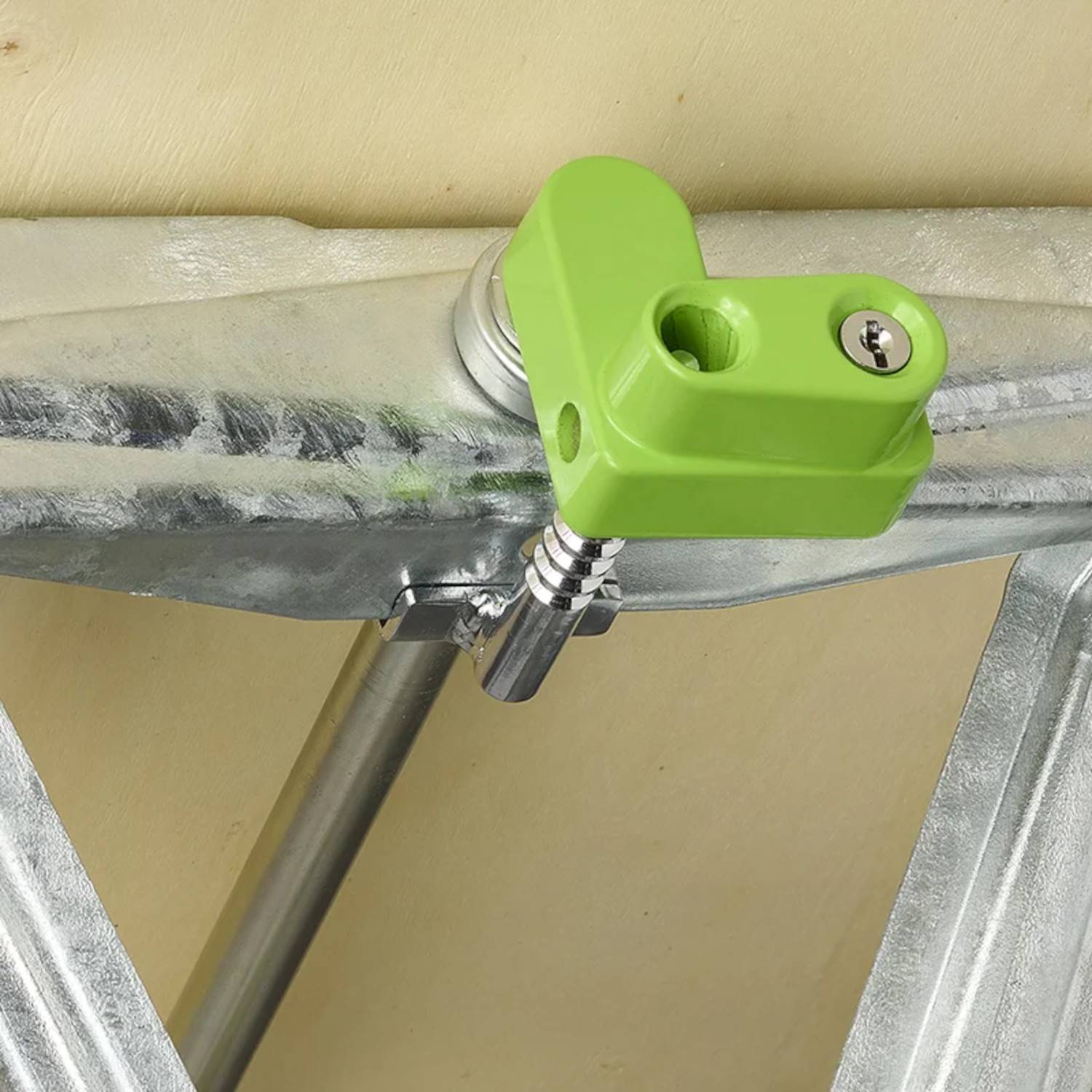 Ein grünes Schloss sichert zwei metallische Streben an der Scharnierverbindung einer Aluminiumleiter und gewährleistet, dass die Leiter stabil und sicher ausgefahren bleibt.