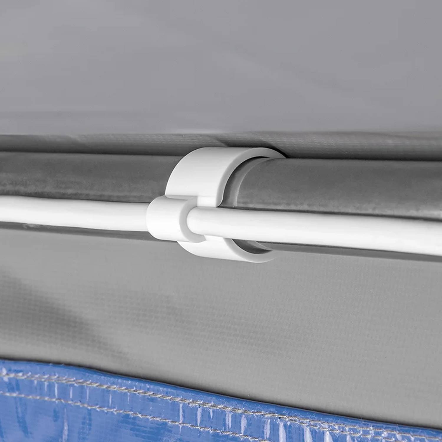 Nahaufnahme eines weißen Kunststoffclips, der eine blaue Poolabdeckung an einem Metallrahmen befestigt und dabei die Platzierung und Funktionalität des Clips hervorhebt.