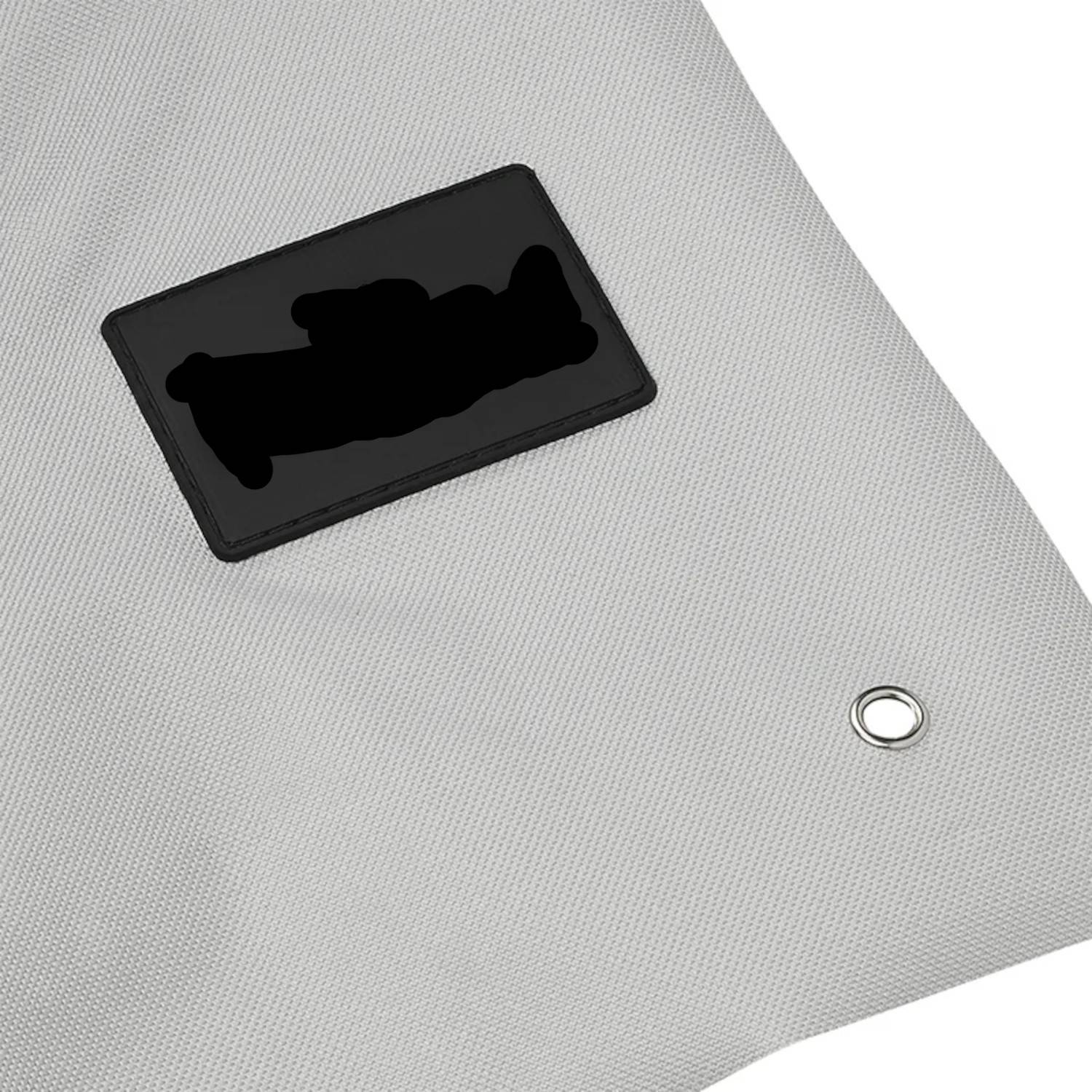 Eine Nahaufnahme einer grauen Plane in der Ecke mit einem schwarzen Flicken und einer Metallöse, die Haltbarkeit und Befestigungspunkte anzeigt.