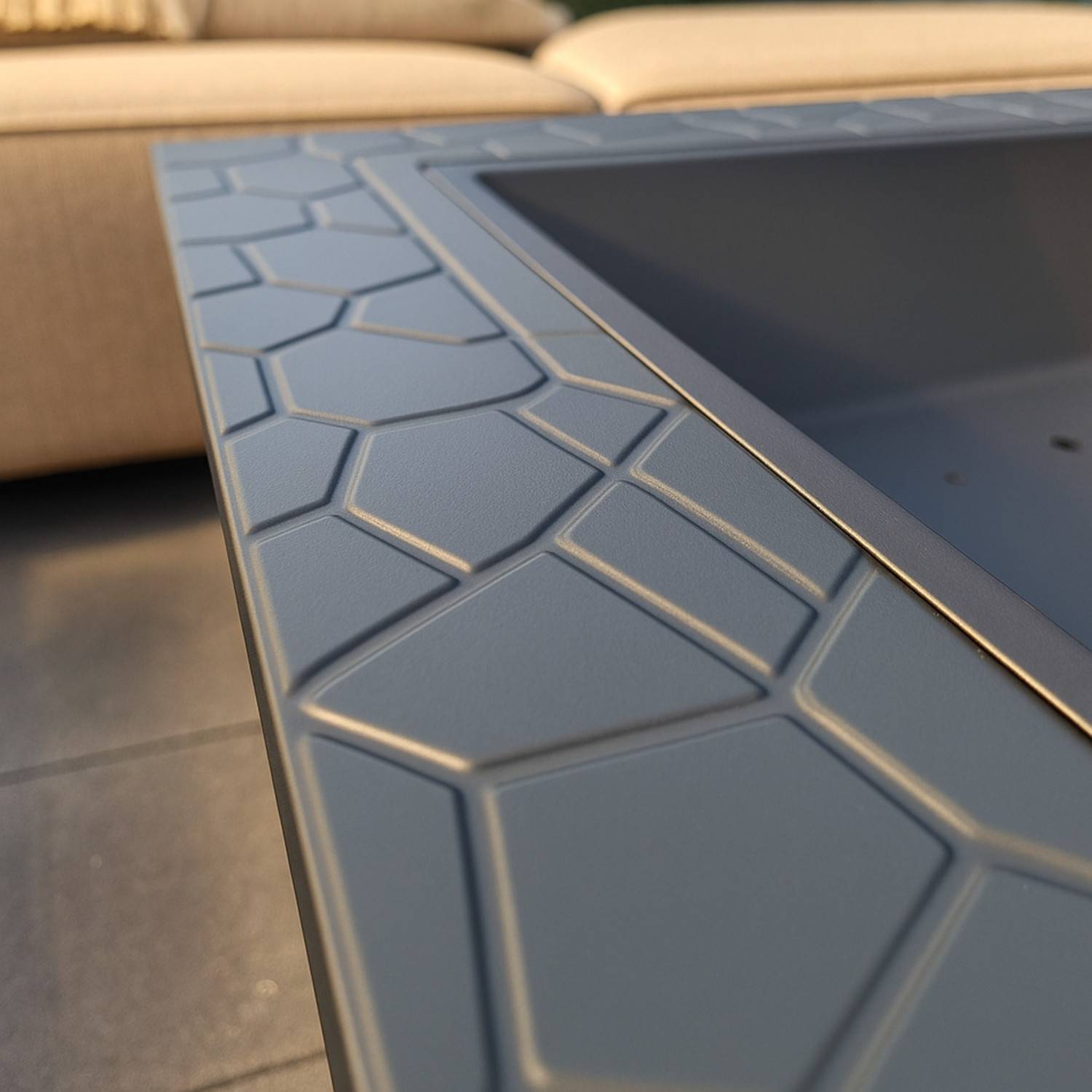 Eine Nahaufnahme einer Tischoberfläche im Freien mit sechseckigem Muster in einer hellen Taupe-Farbe, mit einem Teil eines beigen gepolsterten Sitzes im Hintergrund.