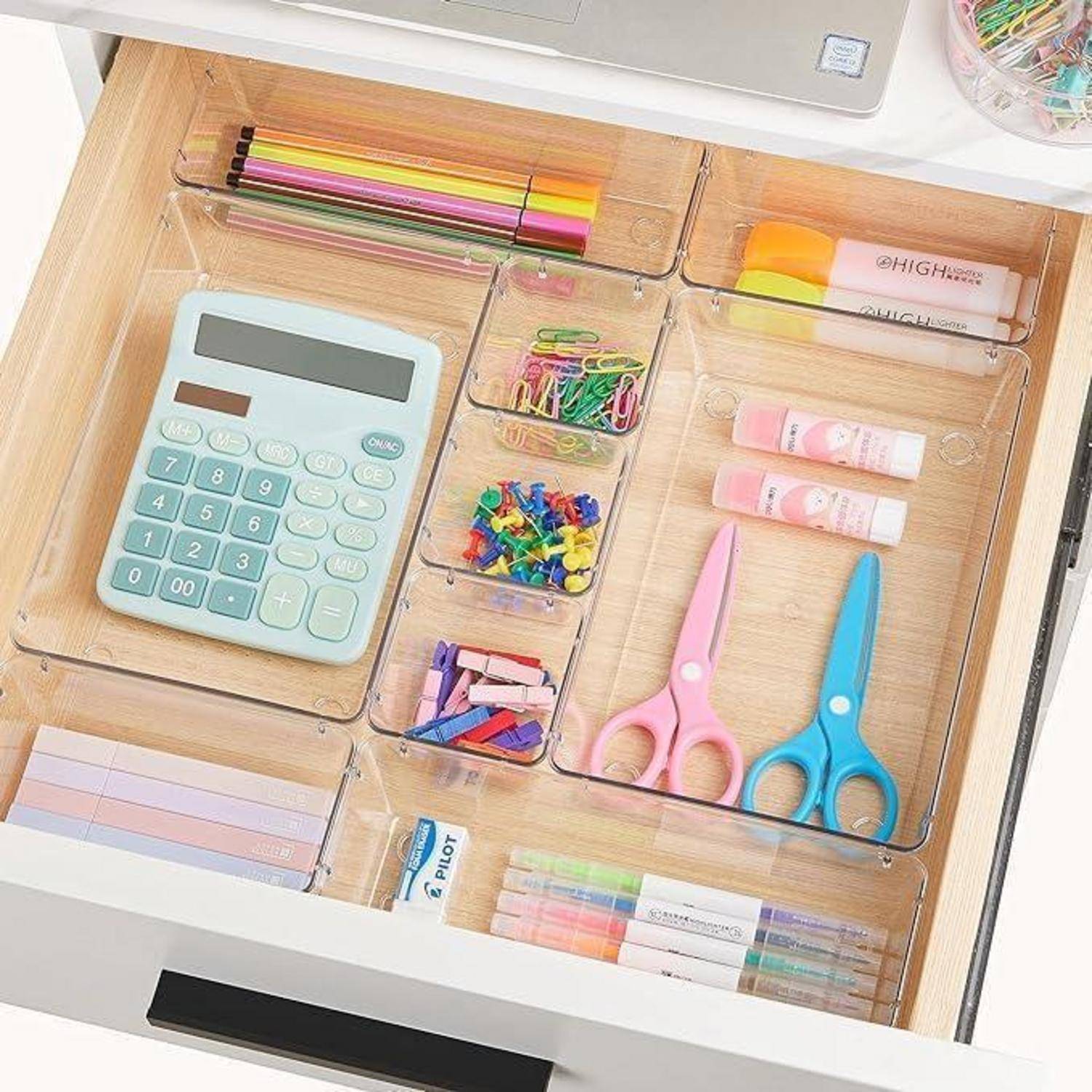 Eine organisierte Schublade mit Fächern, die einen Taschenrechner, bunte Buntstifte, Büroklammern, Pinnwandnadeln, eine Schere und Klebestifte enthält.