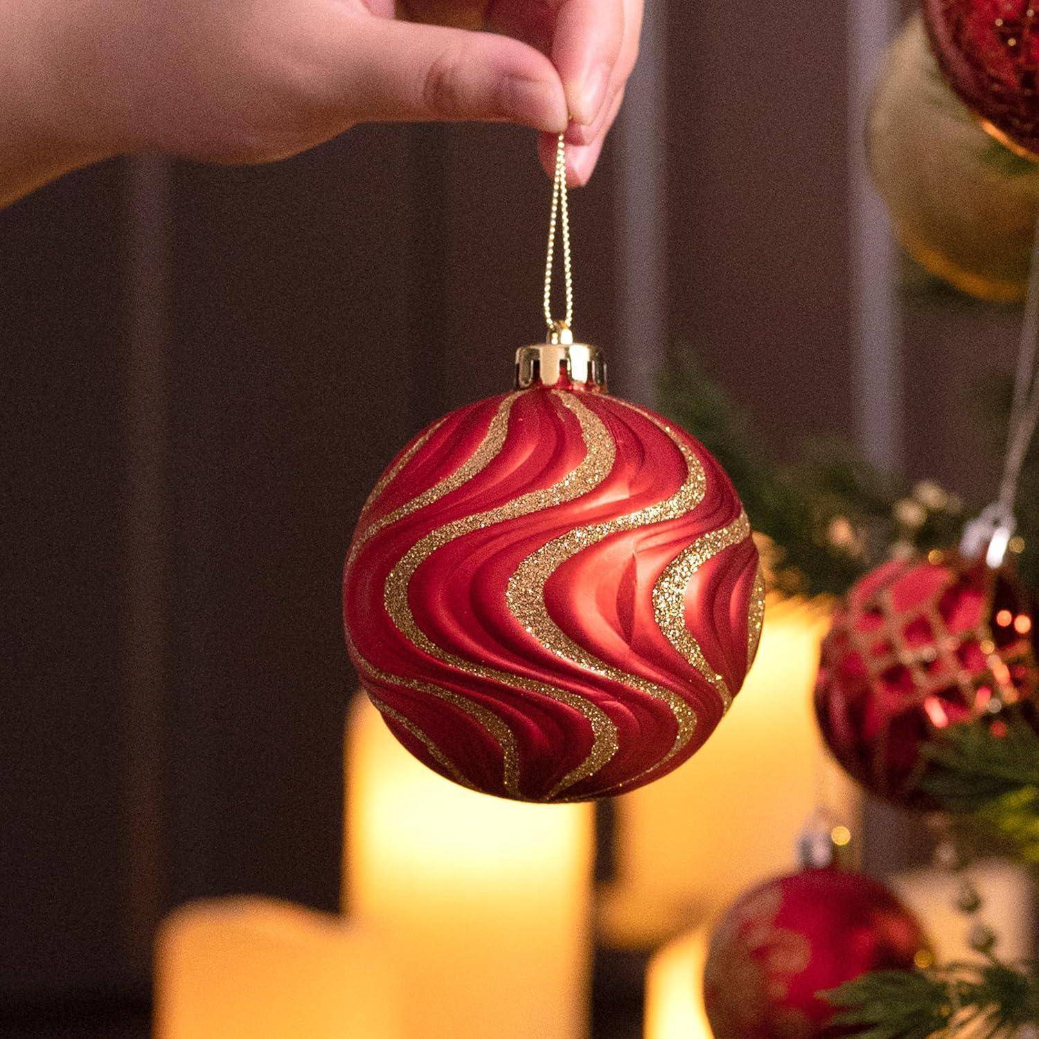 Eine Hand hängt eine rot-goldene Ornament mit Wirbelmustern an einen Weihnachtsbaum, während im Hintergrund sanftes Kerzenlicht schimmert.