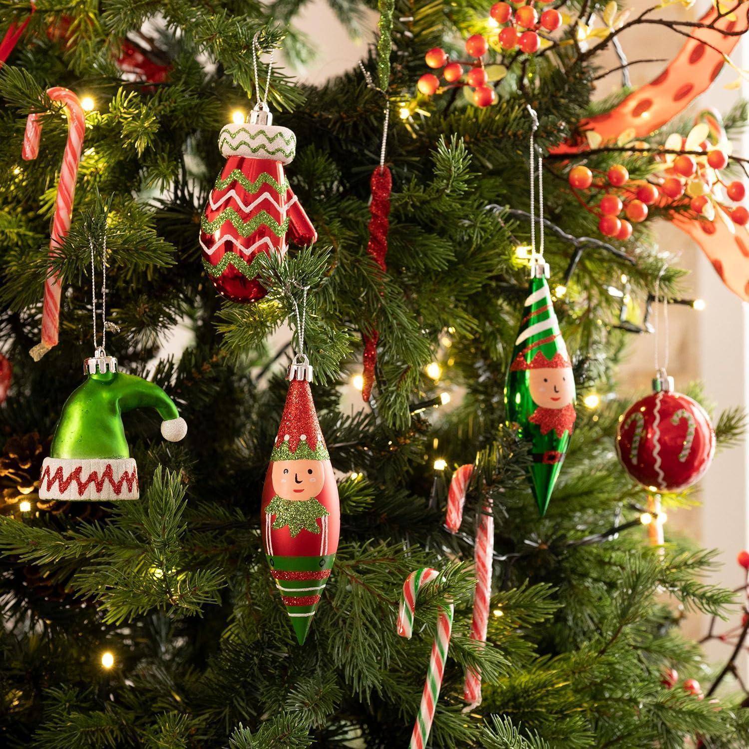 Bunte Weihnachtsschmuck und Zuckerstangen hängen von einem geschmückten Weihnachtsbaum, mit Kugeln in Formen von festlichen Figuren und traditionellen Süßigkeiten.