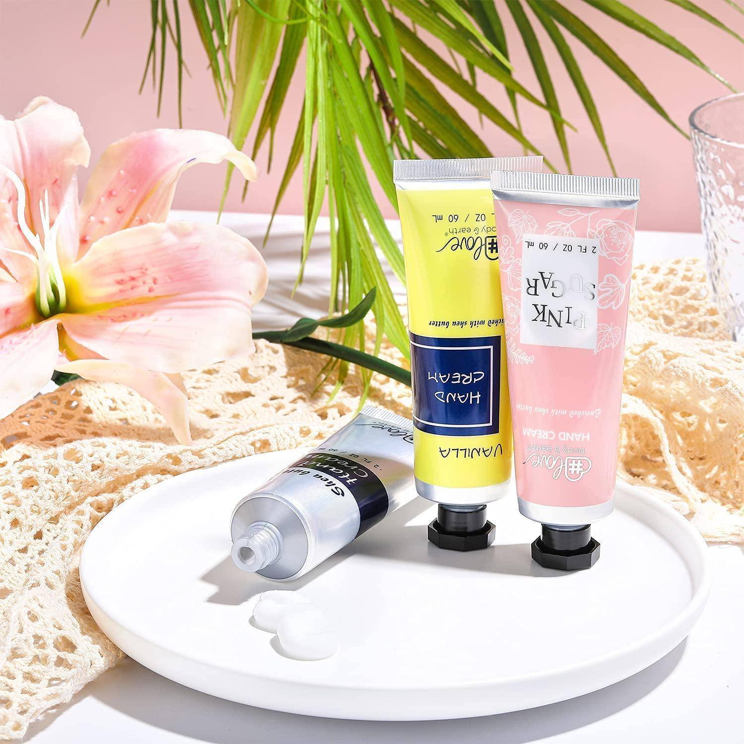 Drei Tuben mit Hautpflegecreme, die mit ‚Gesichtspflege' und ‚Handpflege' beschriftet sind, liegen auf einem weißen Teller mit einer rosa Lilie und Spitzenstoff im Hintergrund.