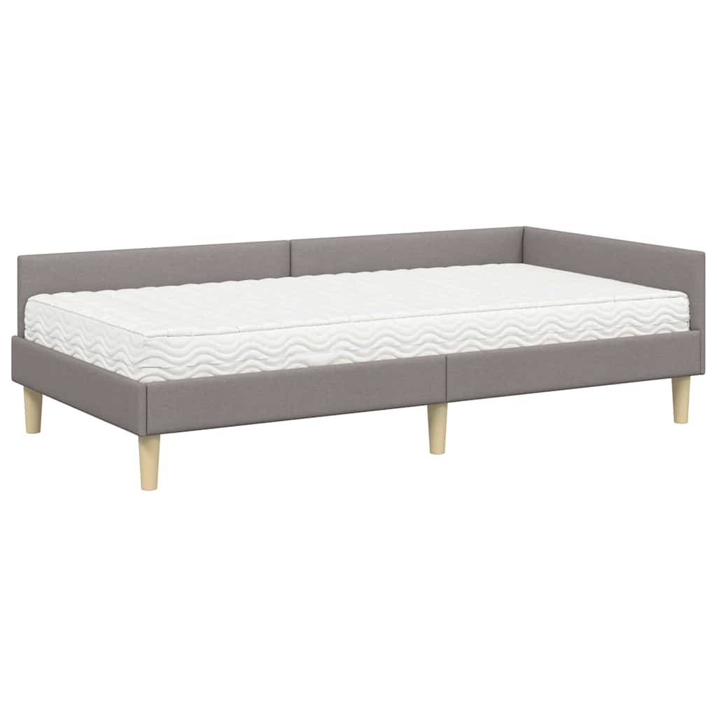 Graues Polster-Tagesbett mit einer weißen Matratze, ausgestattet mit einem minimalistischen Design und hellen Holzbeinen, geeignet für kleine Räume.