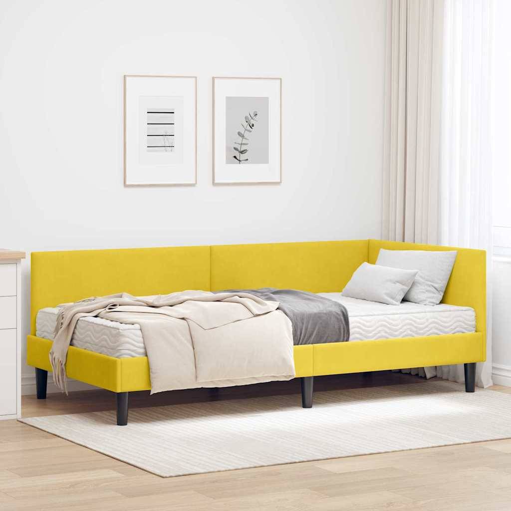Ein modernes Schlafzimmer mit einem gelben Bett, grauer Bettwäsche und einer beigen Wurfdecke in einem hellen Raum mit weißen Wänden und gerahmten Kunstwerken darüber.
