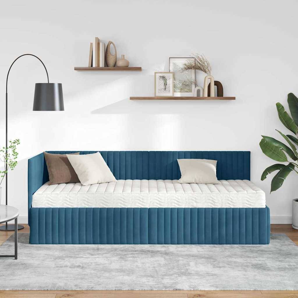 Ein moderner Wohnraum zeigt ein blaues Tagesbett mit weißen und braunen Kissen, eine Stehlampe, einen Teppich, Regale mit Deko und eine Zimmerpflanze.