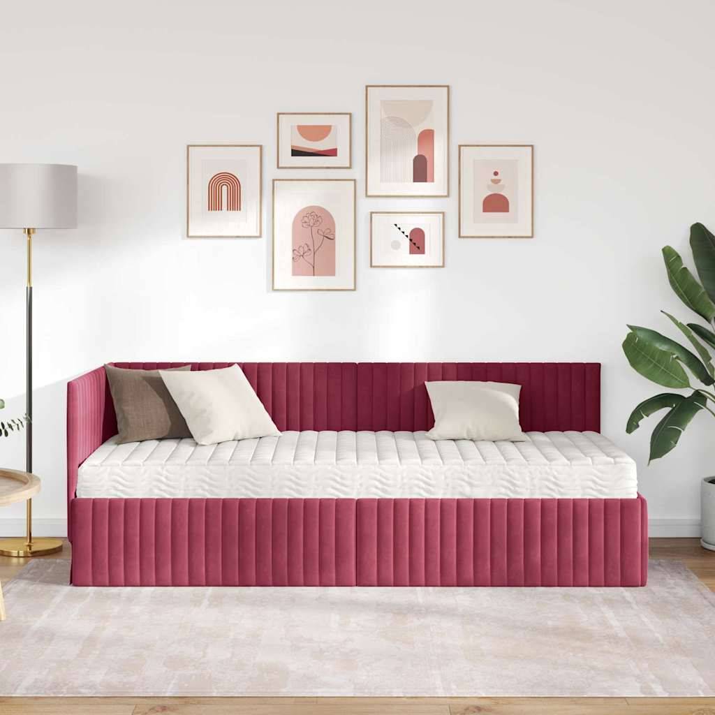 Ein modernes Schlafzimmer zeigt ein mit rotem Polster bezogenes Tagesbett mit zwei weißen Kissen, eine Galeriewand mit abstrakter Kunst, eine Stehlampe und eine Zimmerpflanze.
